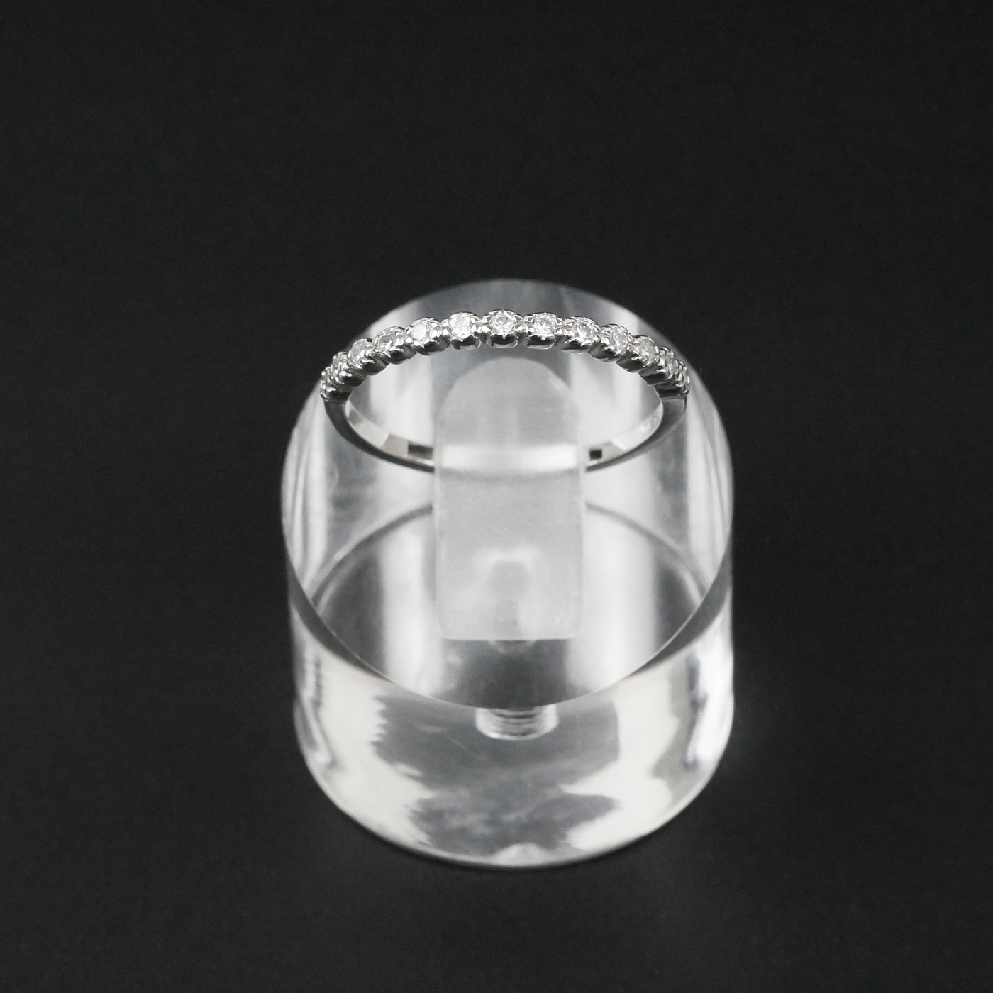 Silver ring with CZ's on a clear stand against a black background