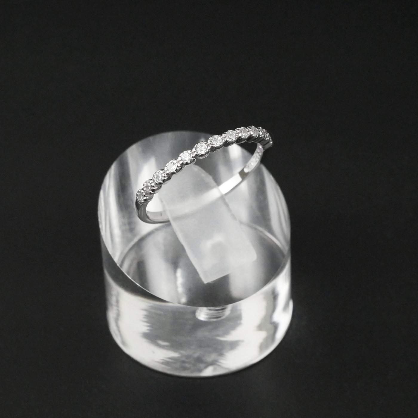 Silver ring with CZ's on a clear stand against a black background