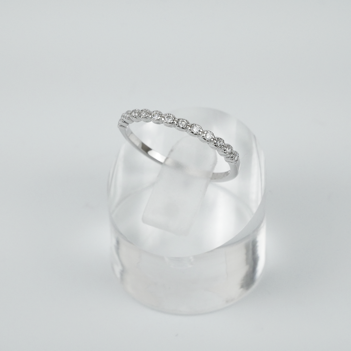 Silver ring with small cubic zirconias on a clear stand against a light gray background