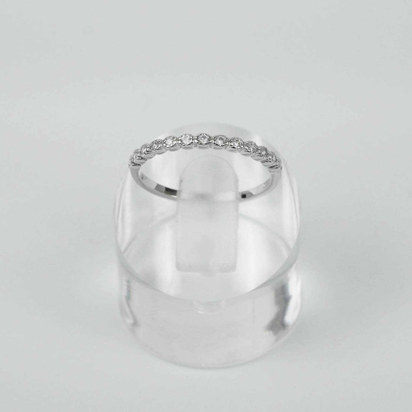 Silver ring with small cubic zirconias on a clear stand against a light gray background
