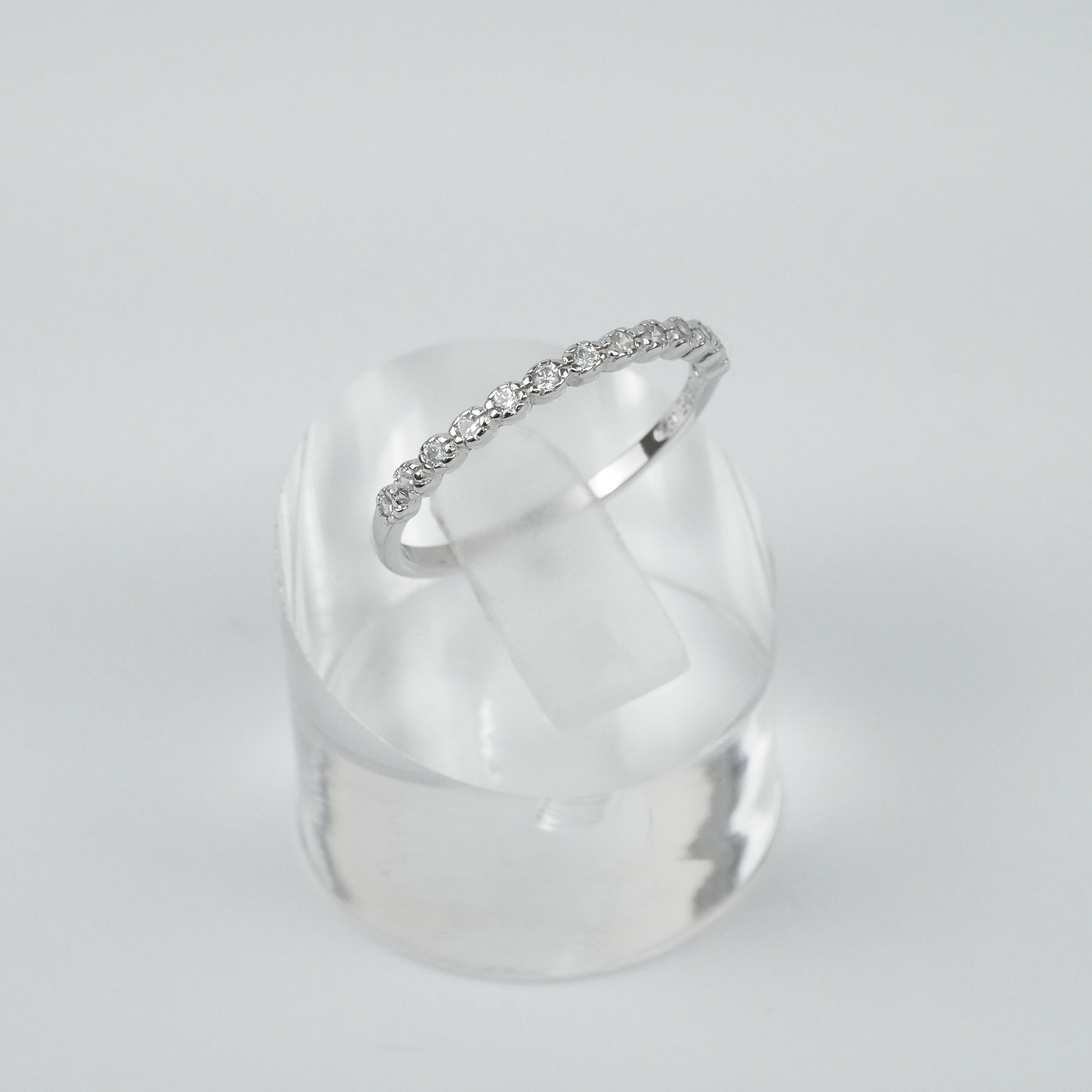 Silver ring with small cubic zirconias on a clear stand against a light gray background