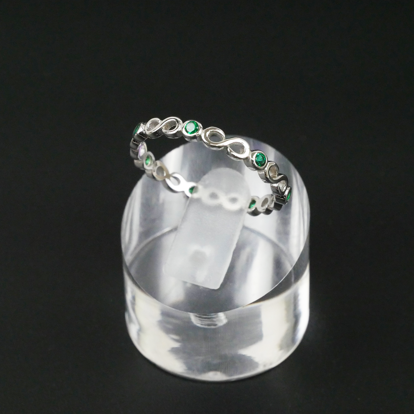 Silver ring with green gemstones on a clear stand against a black background