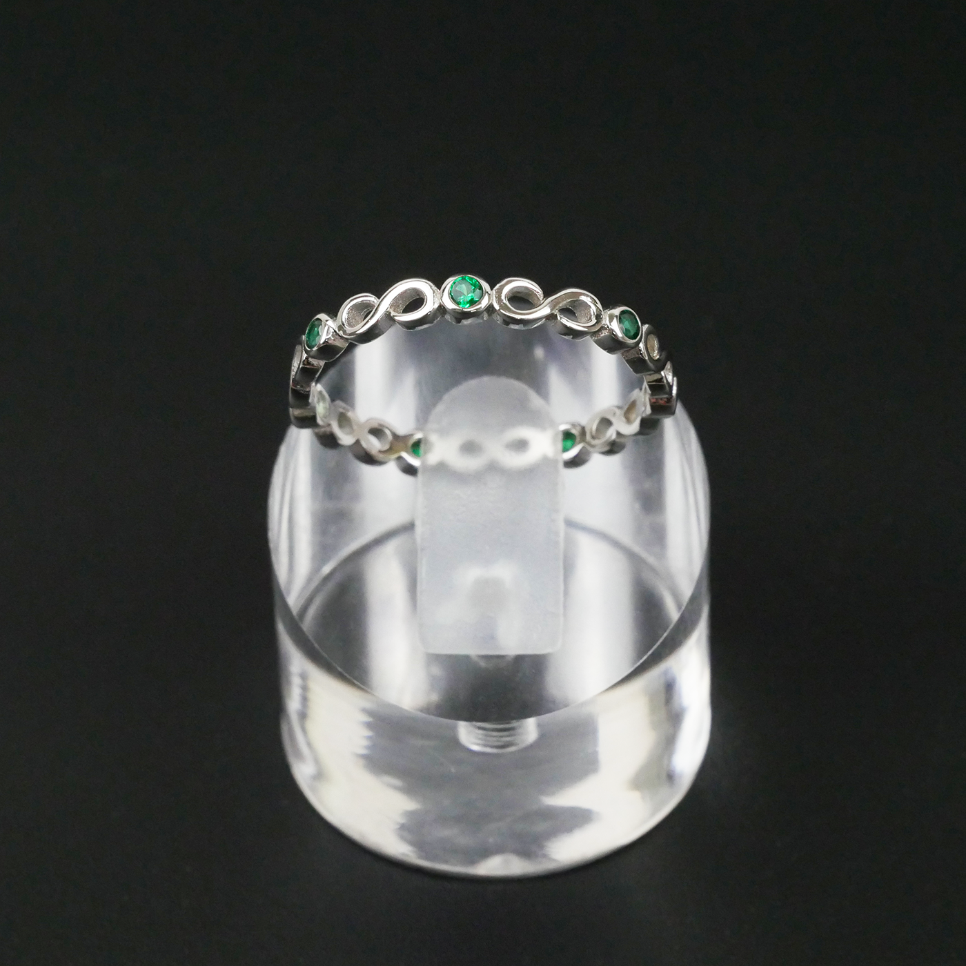 Silver ring with green gemstones on a clear stand against a black background