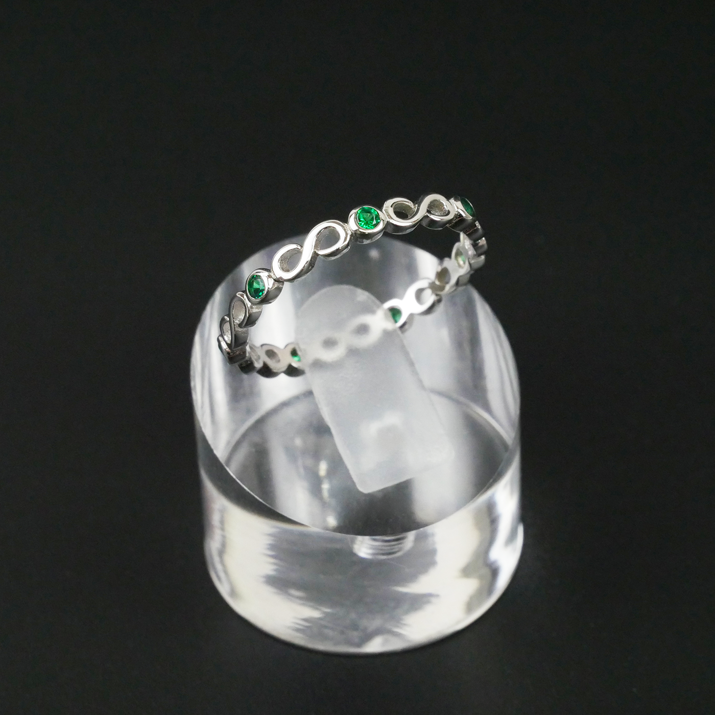 Silver ring with green gemstones on a clear stand against a black background