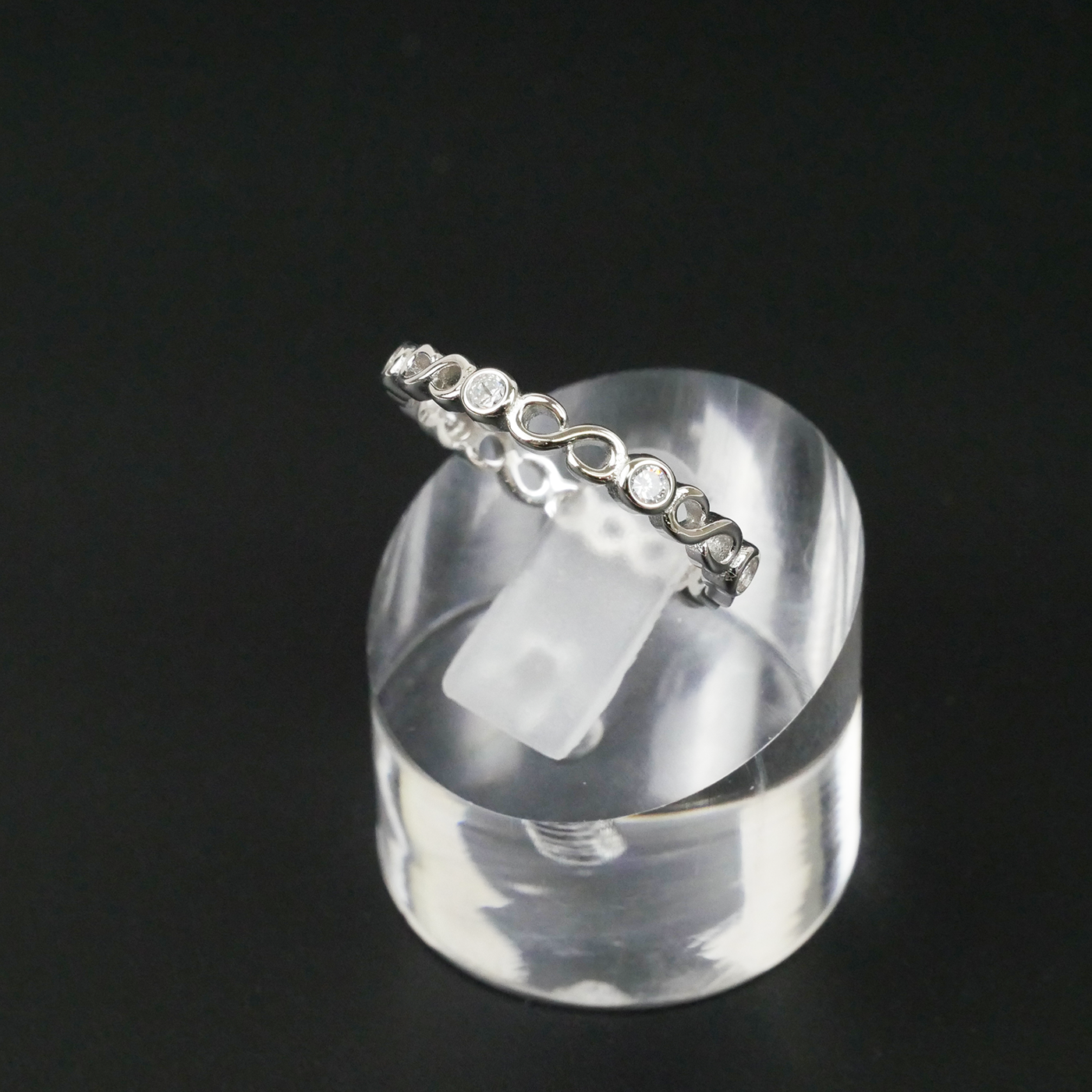 Silver ring with small stones on a clear stand against a black background