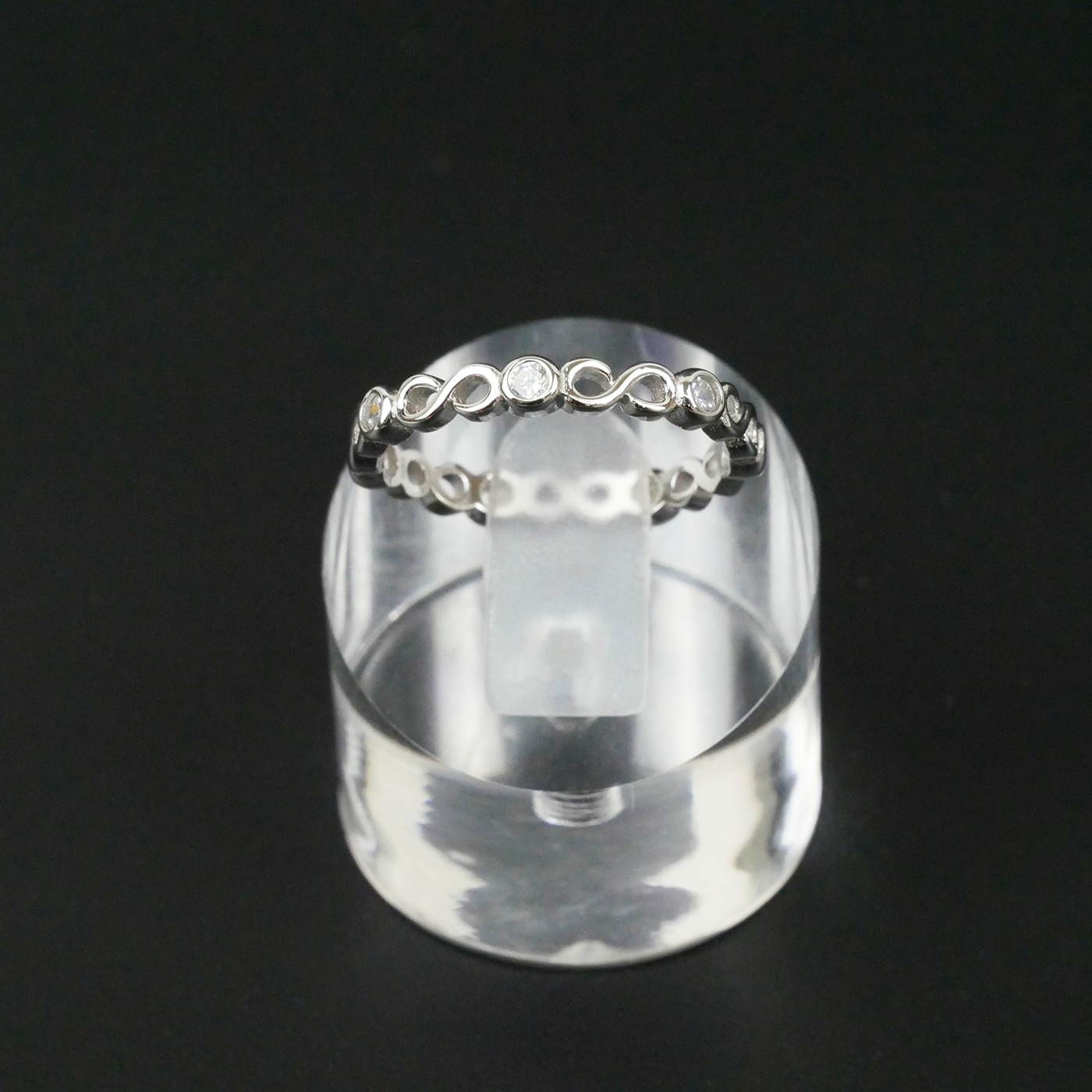 Silver ring with small stones on a clear stand against a black background