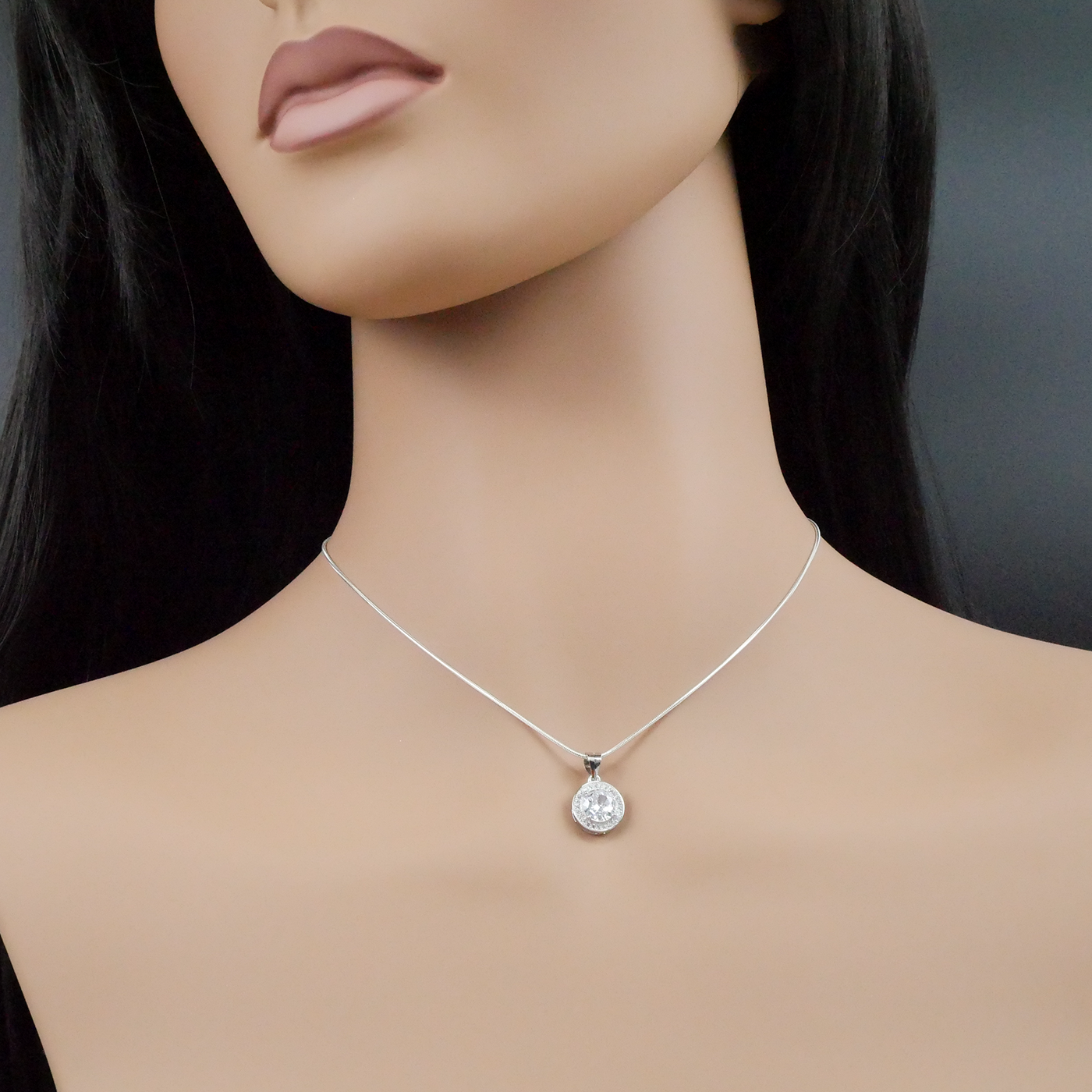 Mannequin wearing a silver necklace with a round pendant on a dark background