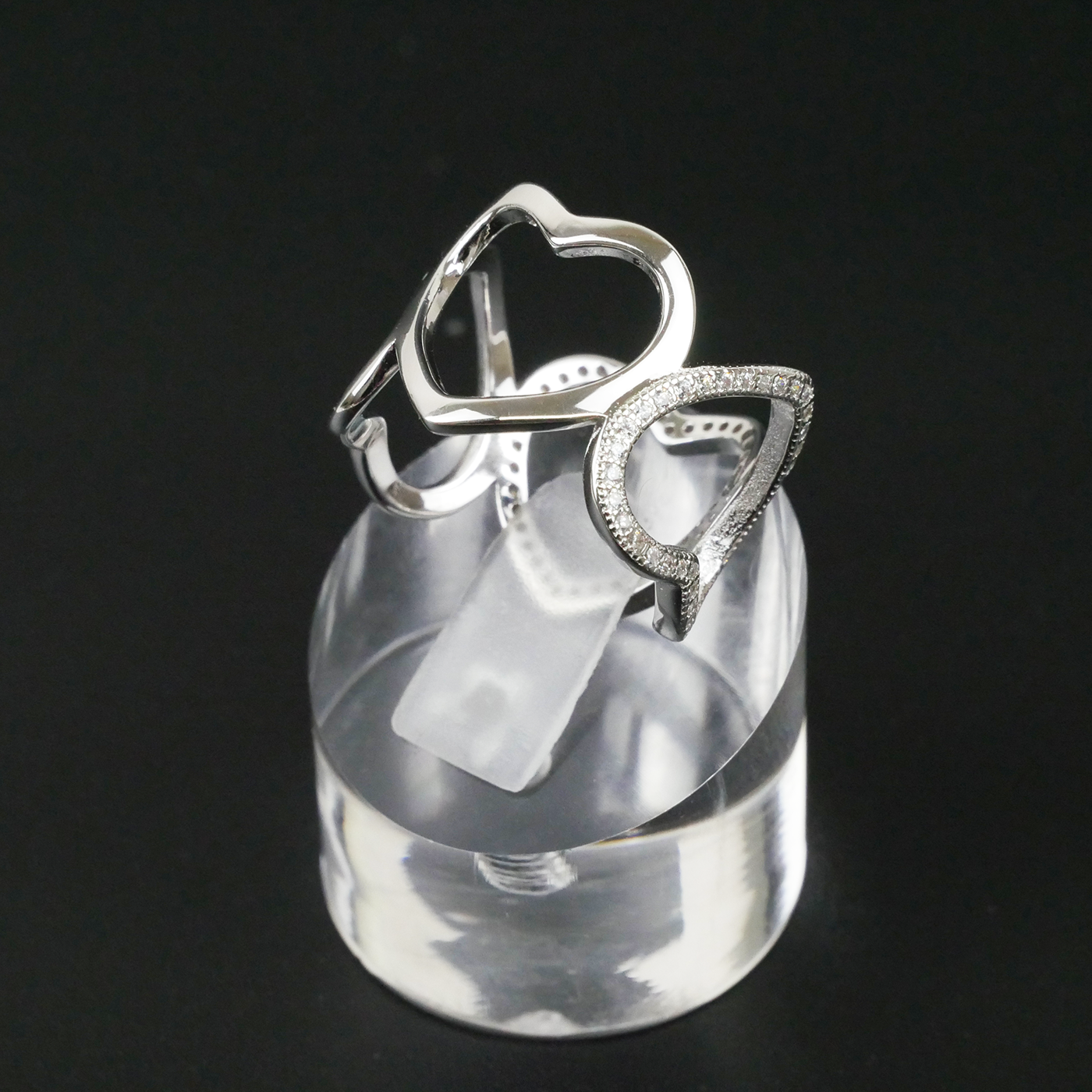 Silver ring with heart design on a clear stand against a black background