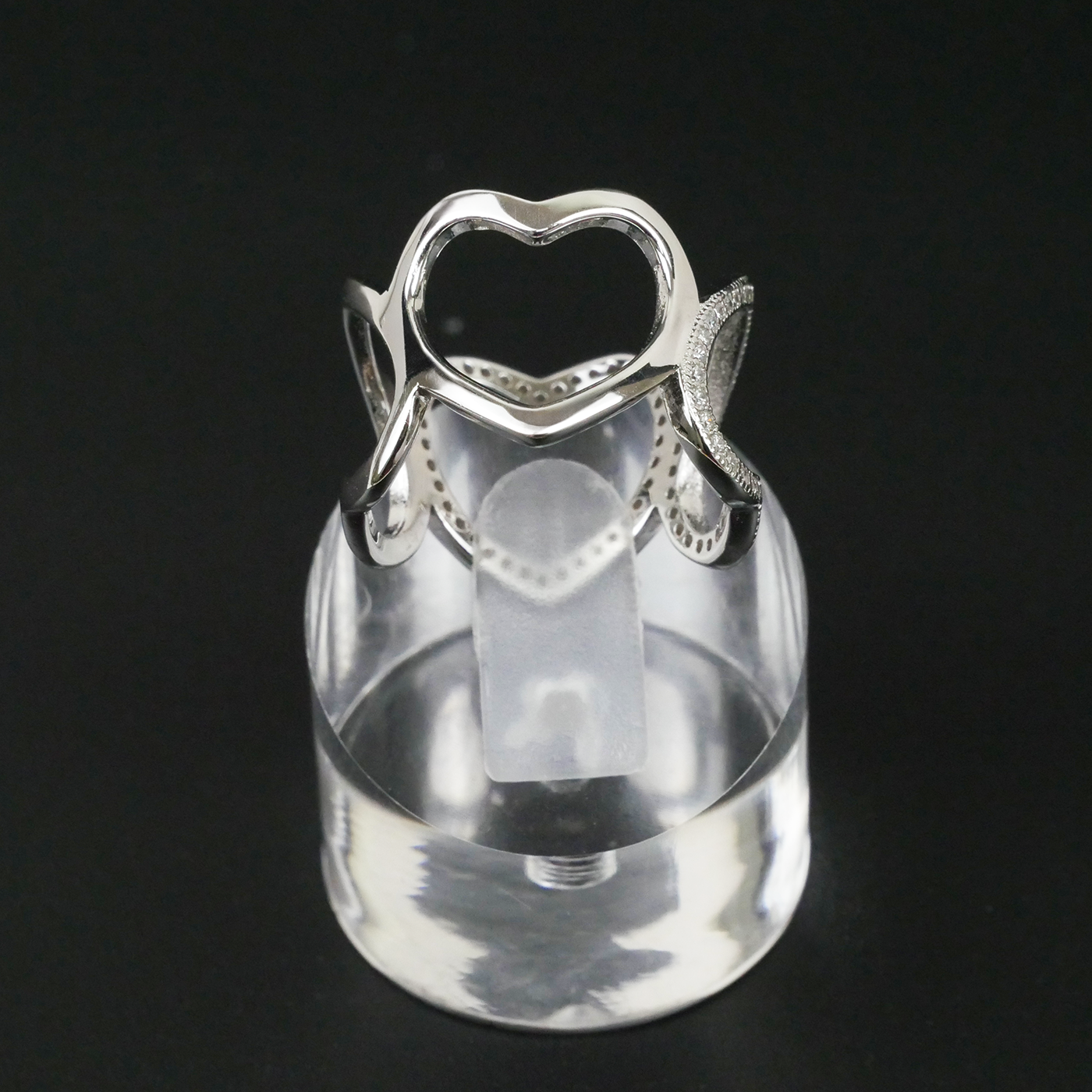 Silver ring with heart design on a clear stand against a black background