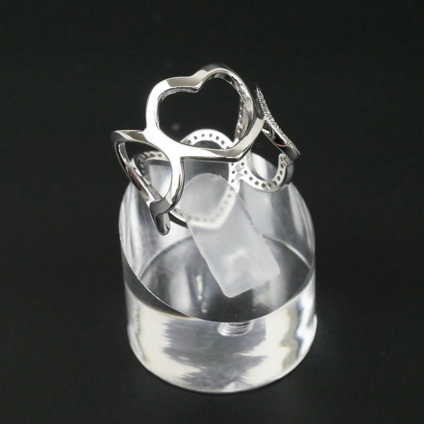 Silver ring with heart design on a clear stand against a black background