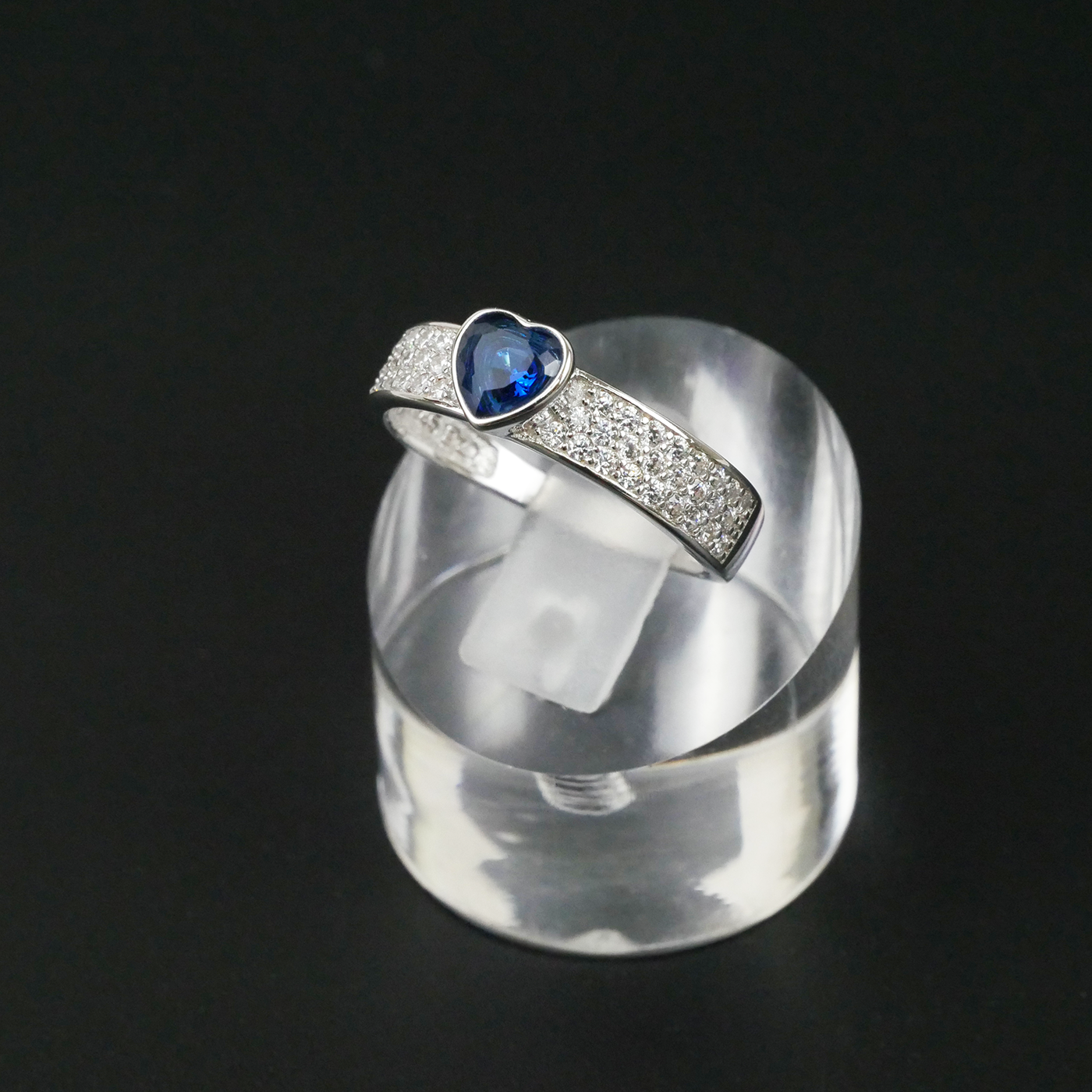 Silver ring with a blue gemstone on a clear stand against a black background