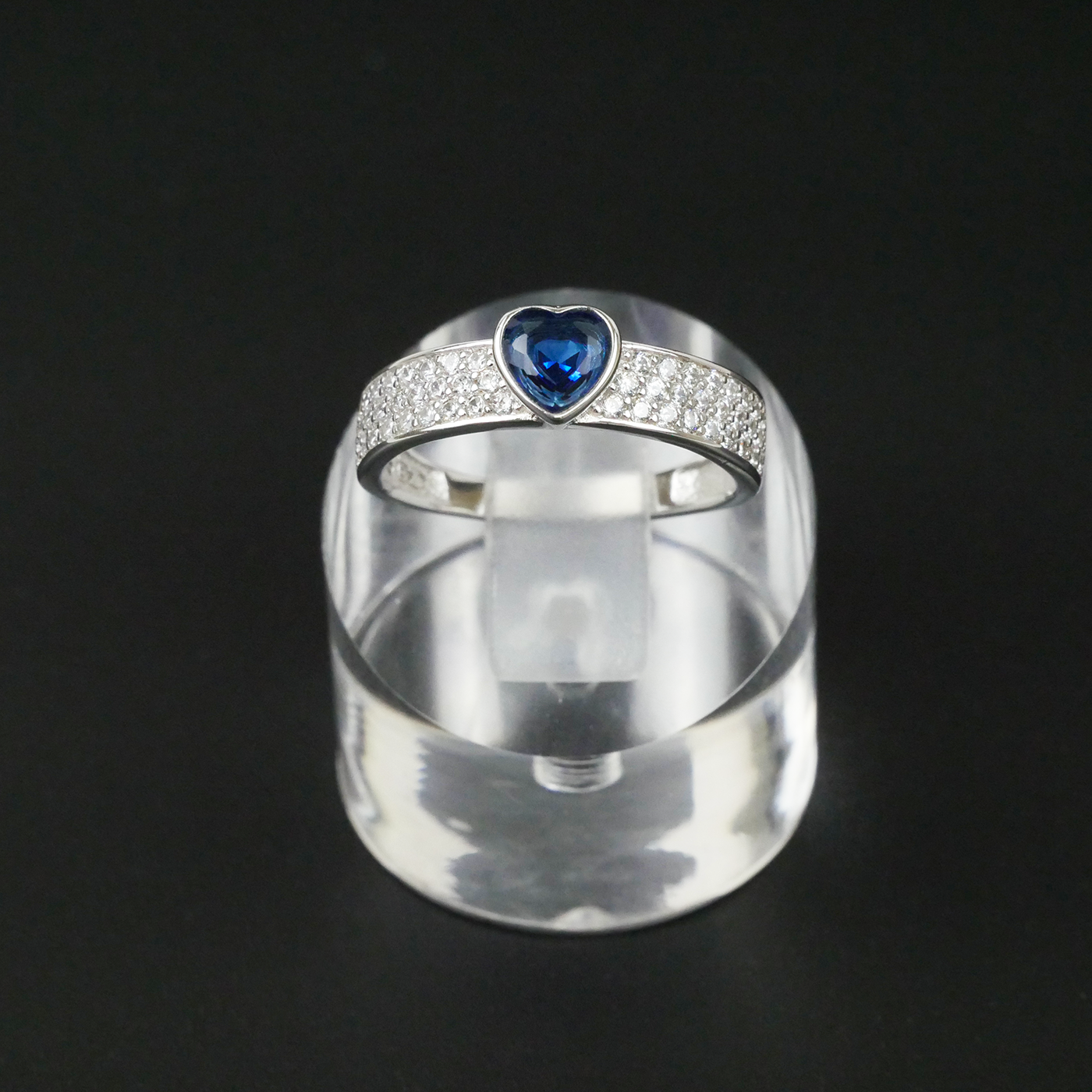 Silver ring with a blue gemstone on a clear stand against a black background
