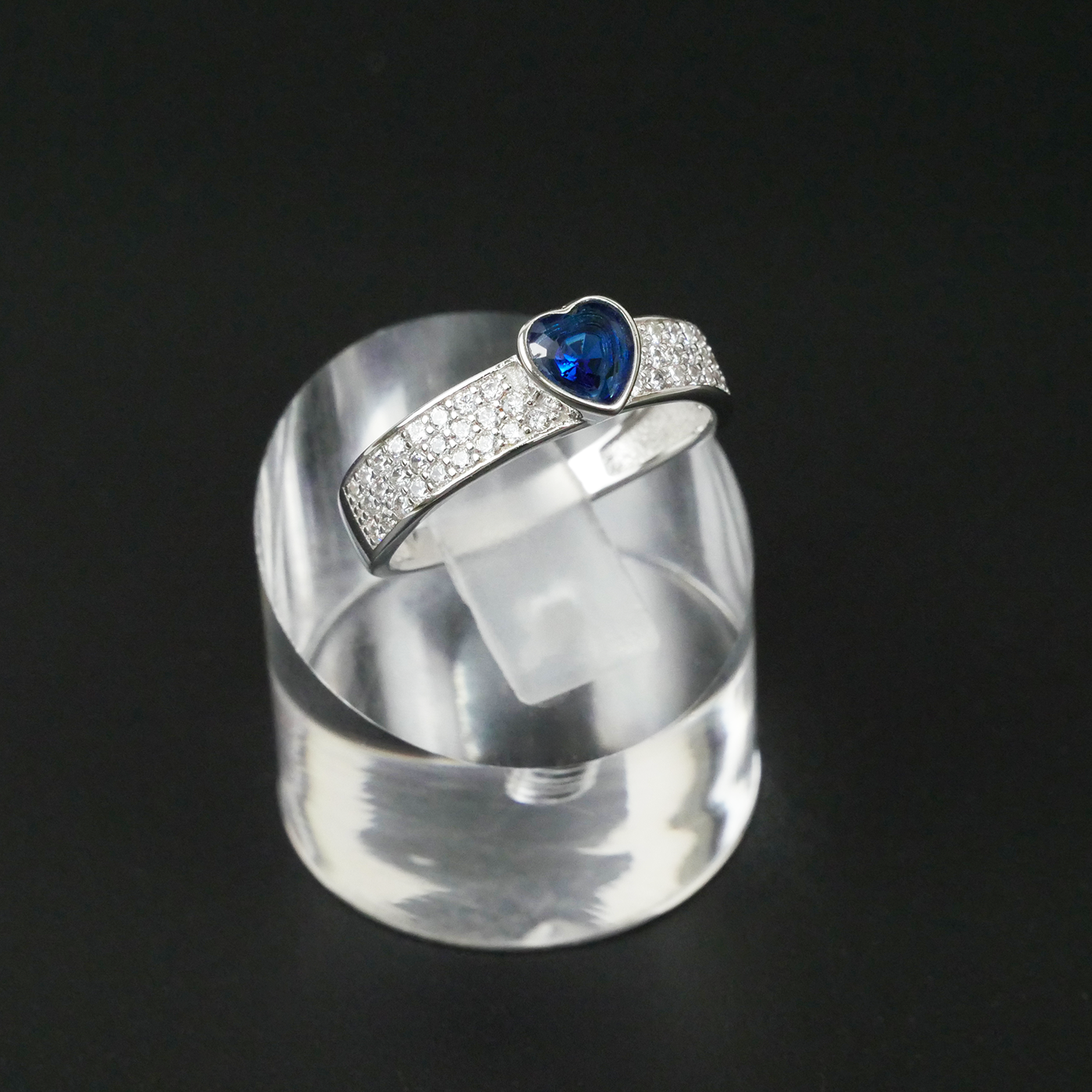 Silver ring with a blue gemstone on a clear stand against a black background