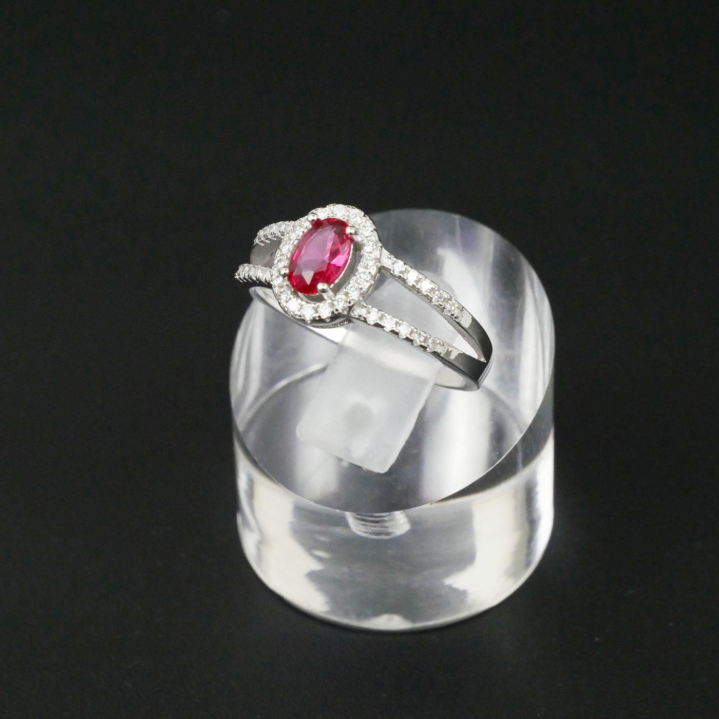 Silver ring with a red gemstone on a clear stand against a black background