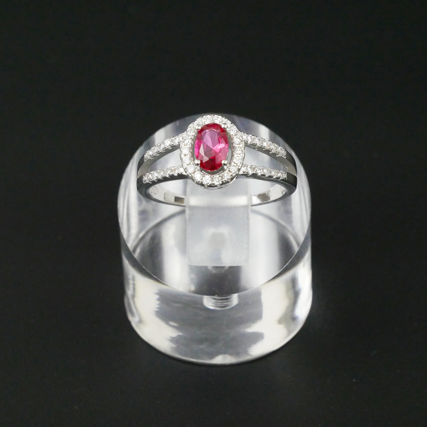 Silver ring with a red gemstone on a clear stand against a black background