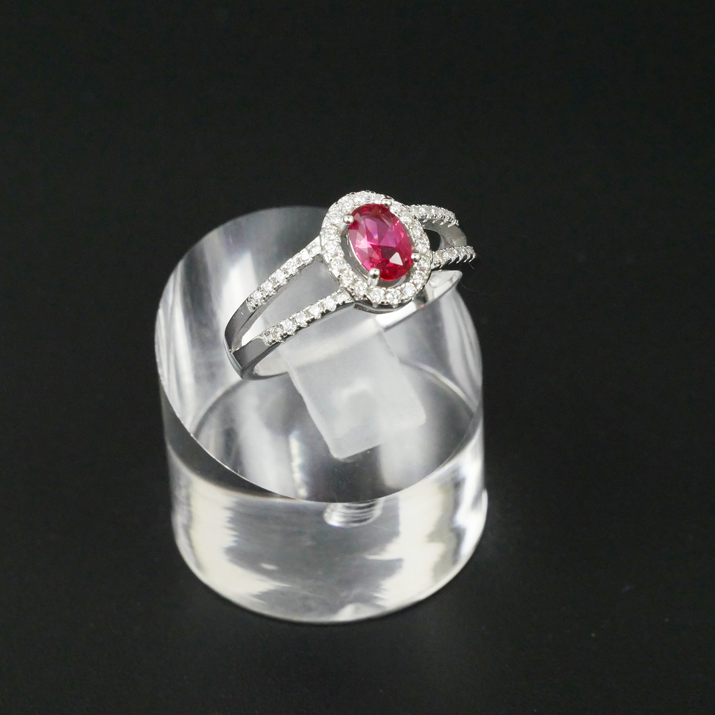Silver ring with a red gemstone on a clear stand against a black background