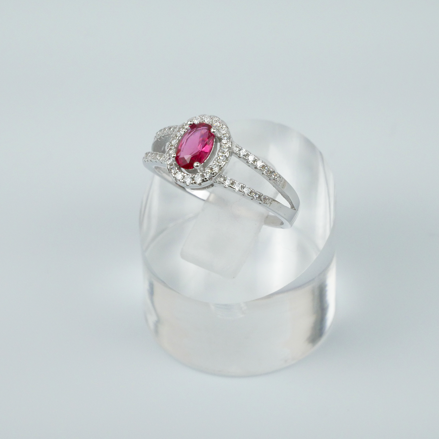 Silver ring with a red gemstone on a clear stand against a light grey background