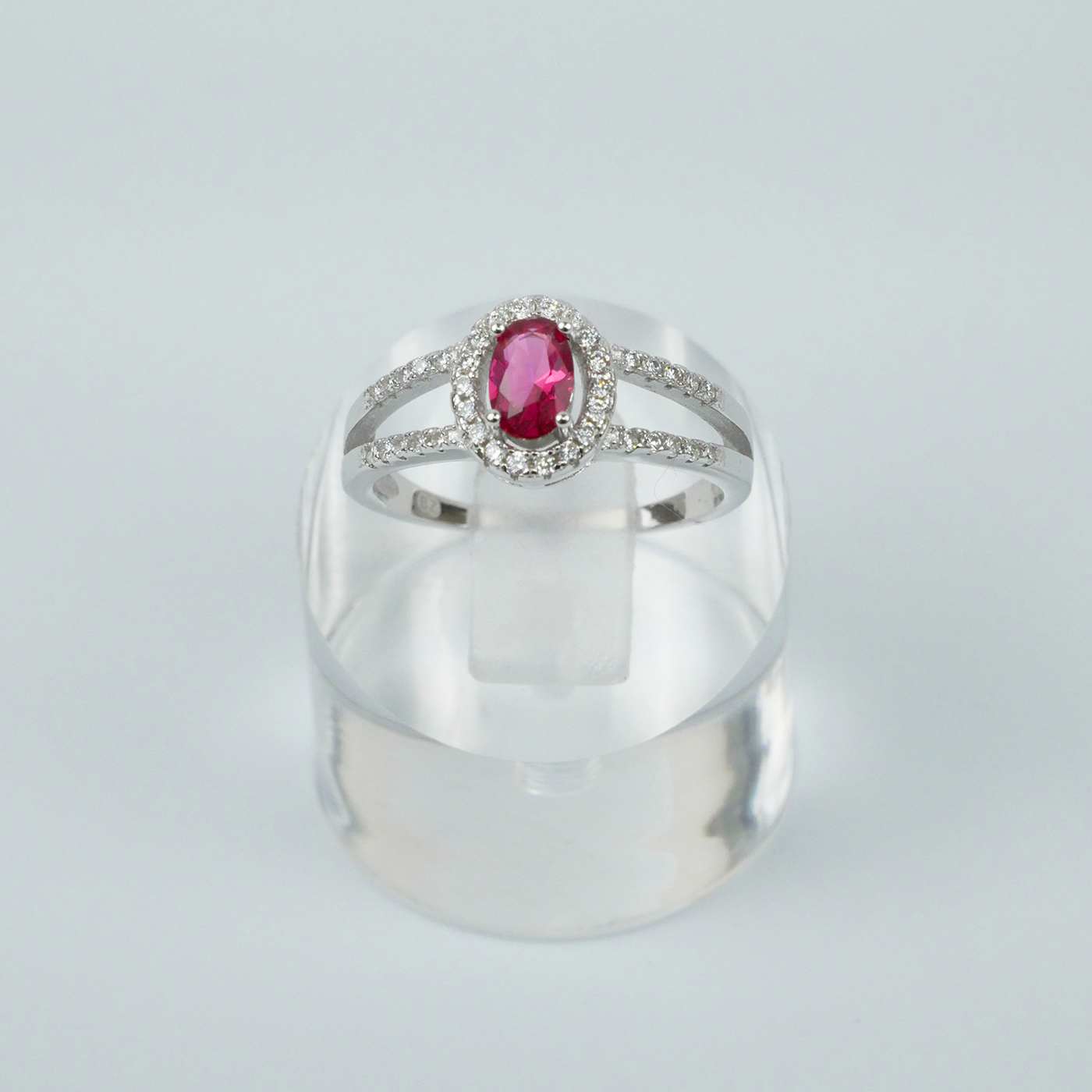 Silver ring with a red gemstone on a clear stand against a light grey background