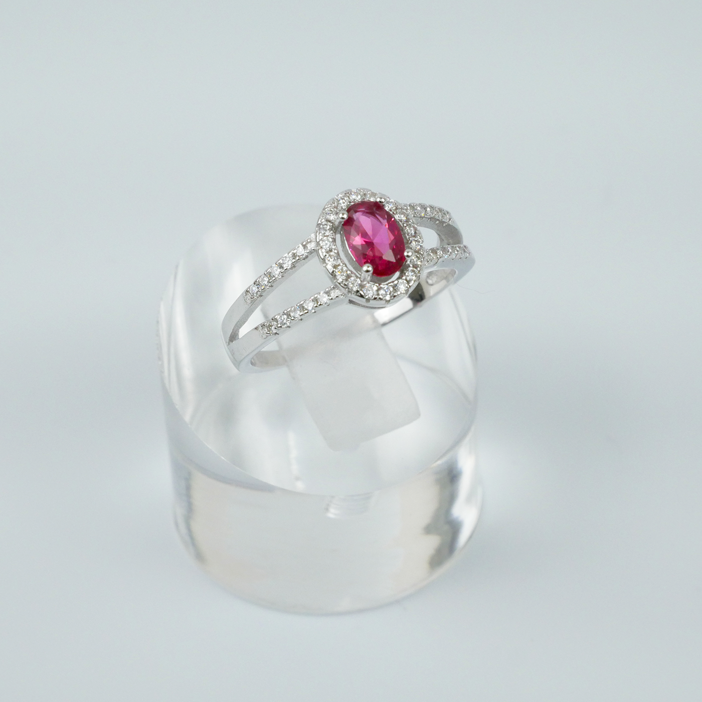 Silver ring with a red gemstone on a clear stand against a light grey background