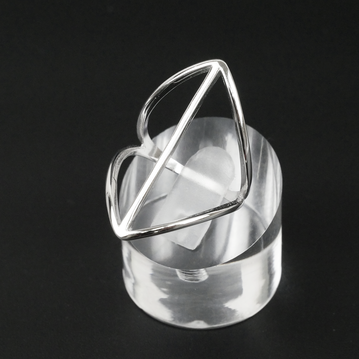 Silver ring with geometric design on a clear stand against a black background