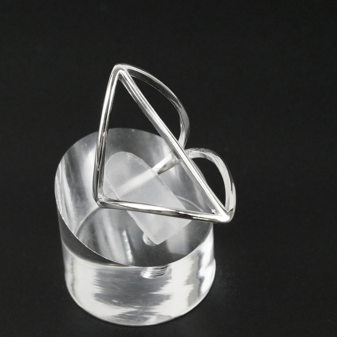Silver ring with geometric design on a clear stand against a black background