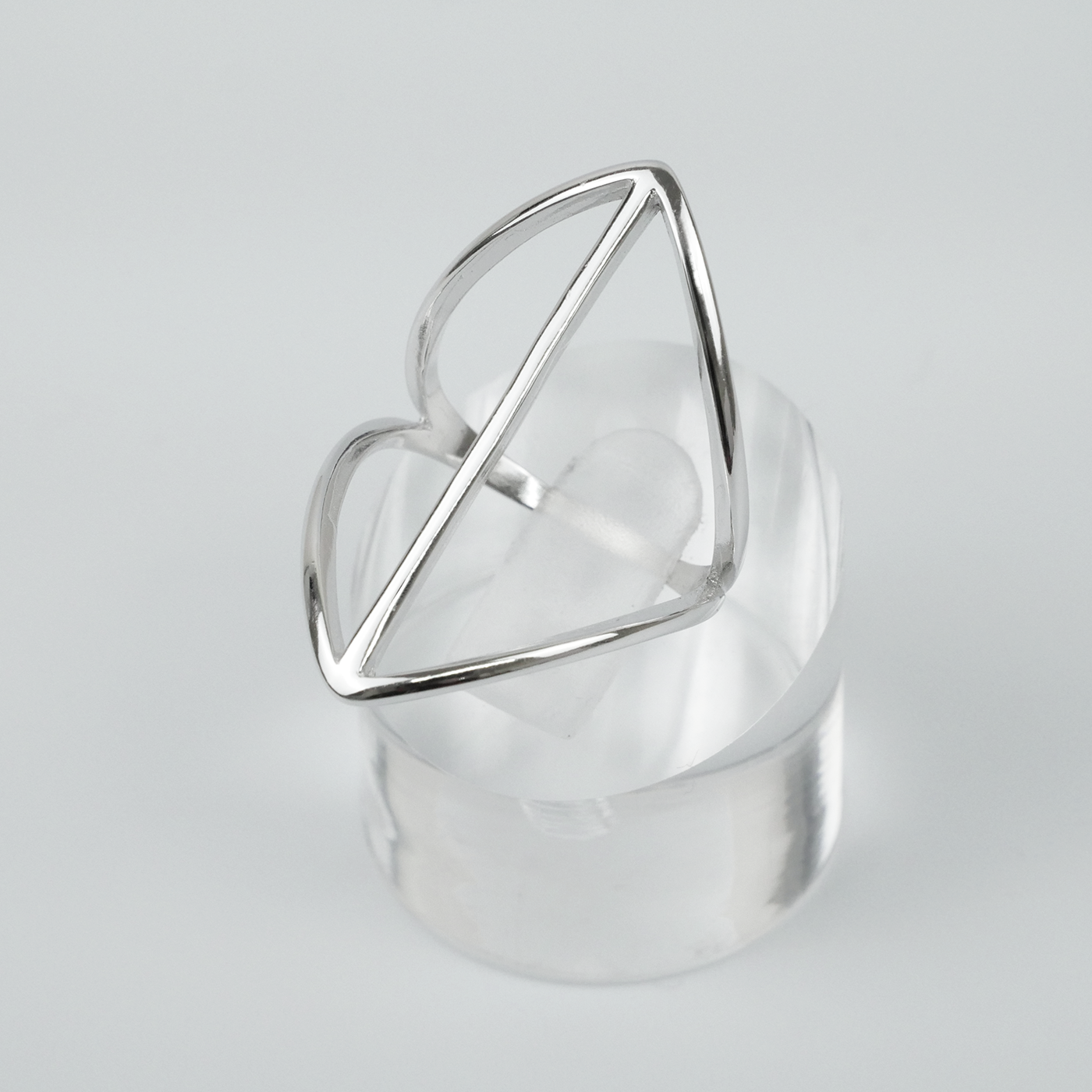 Silver geometric ring on a clear stand with a light gray background