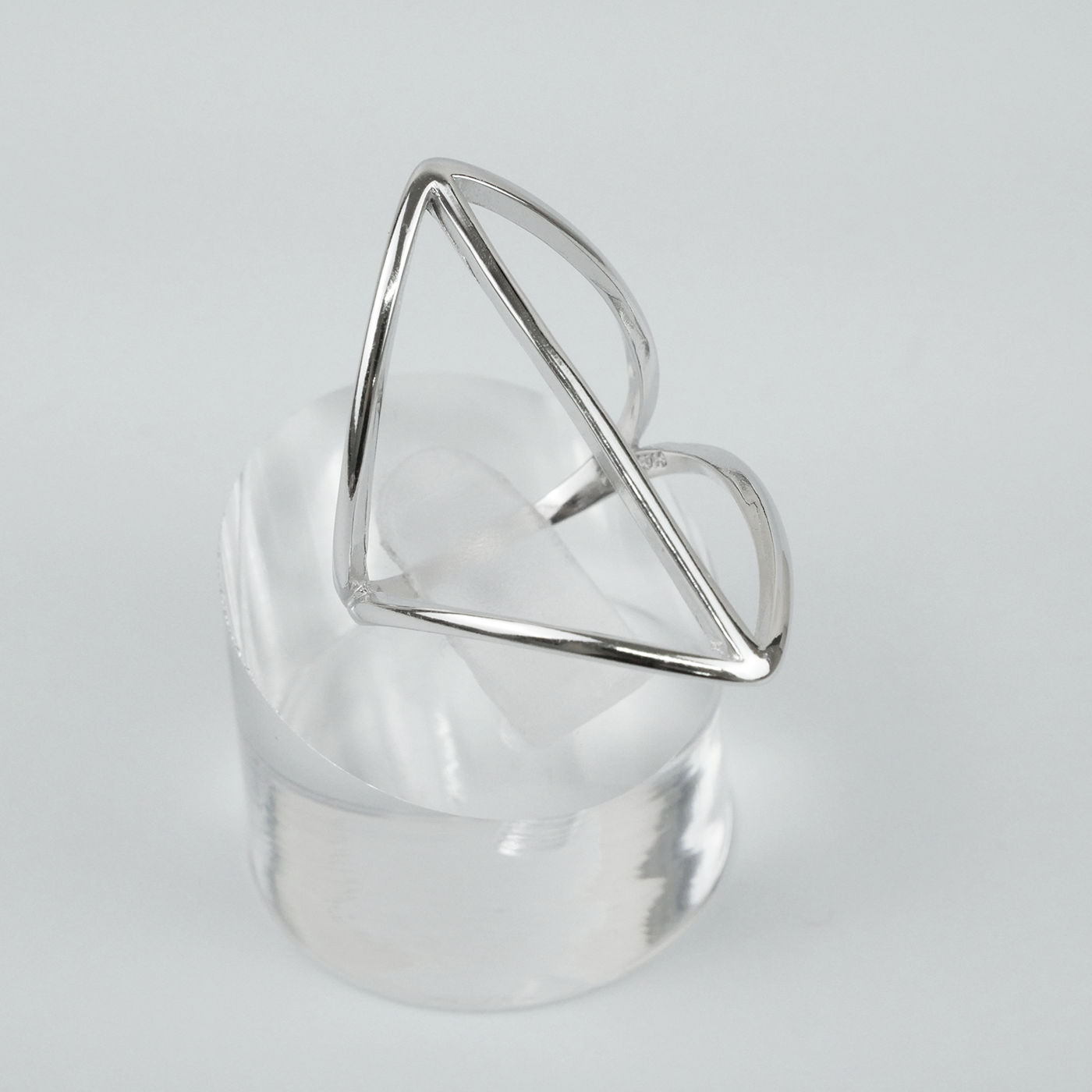 Silver geometric ring on a clear stand against a light gray background