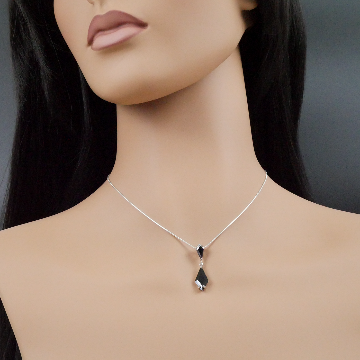 Mannequin wearing a silver necklace with a black pendant on a dark background