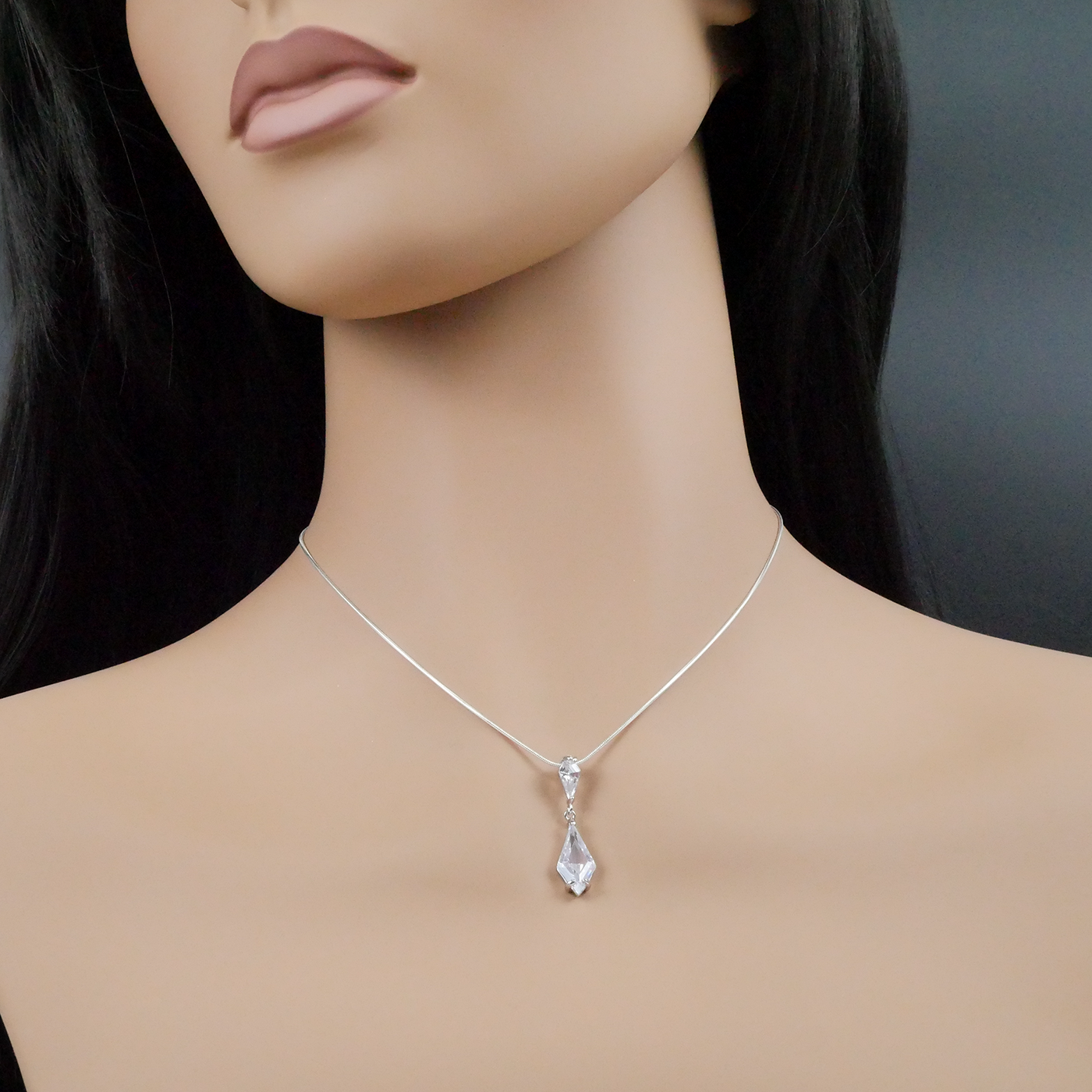 Mannequin wearing a silver necklace with a teardrop pendant on a dark background