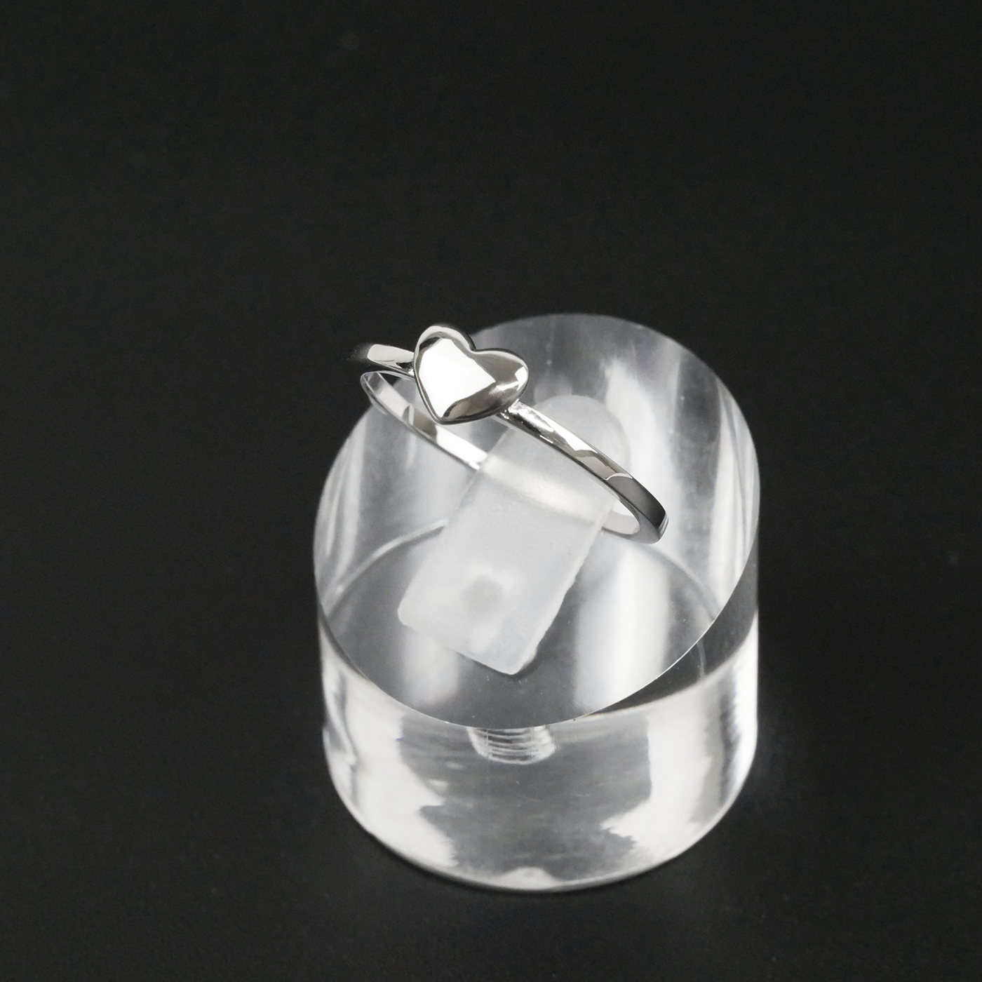 Silver ring with a heart design on a clear stand against a black background