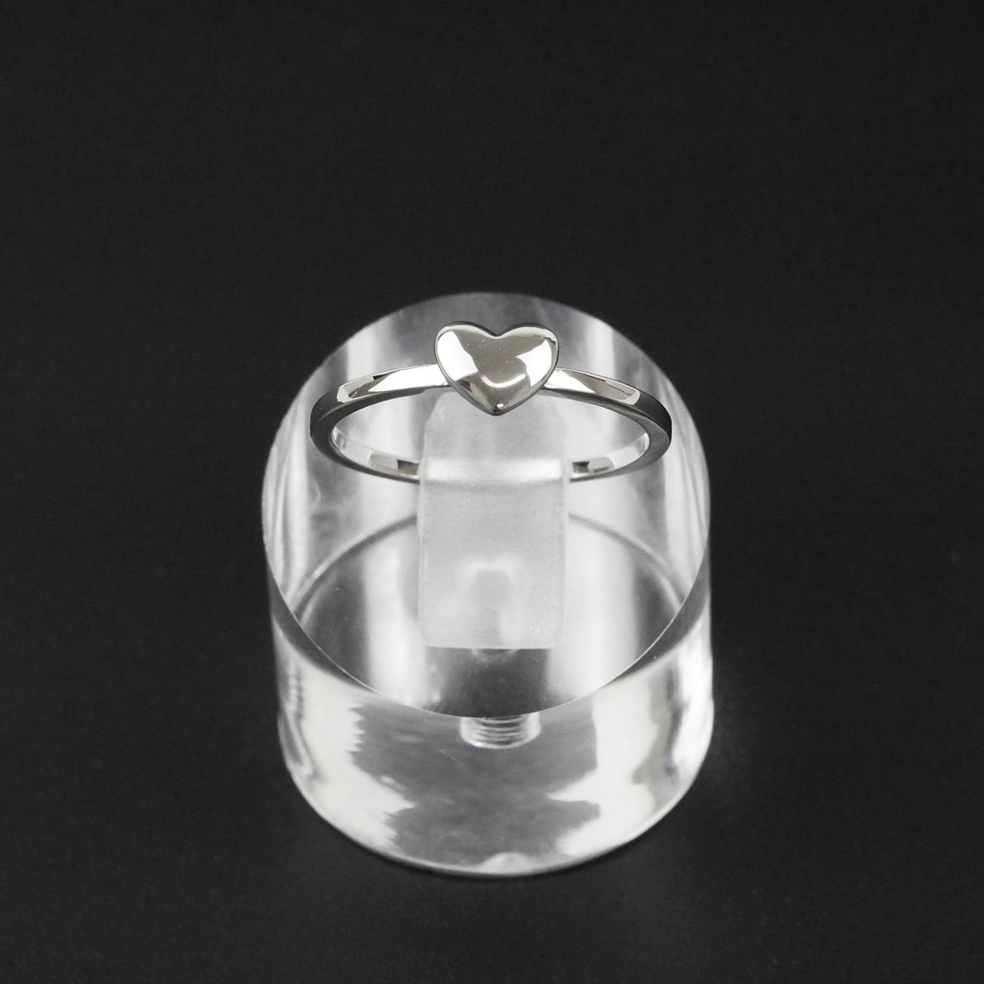 Silver ring with a heart design on a clear stand against a black background