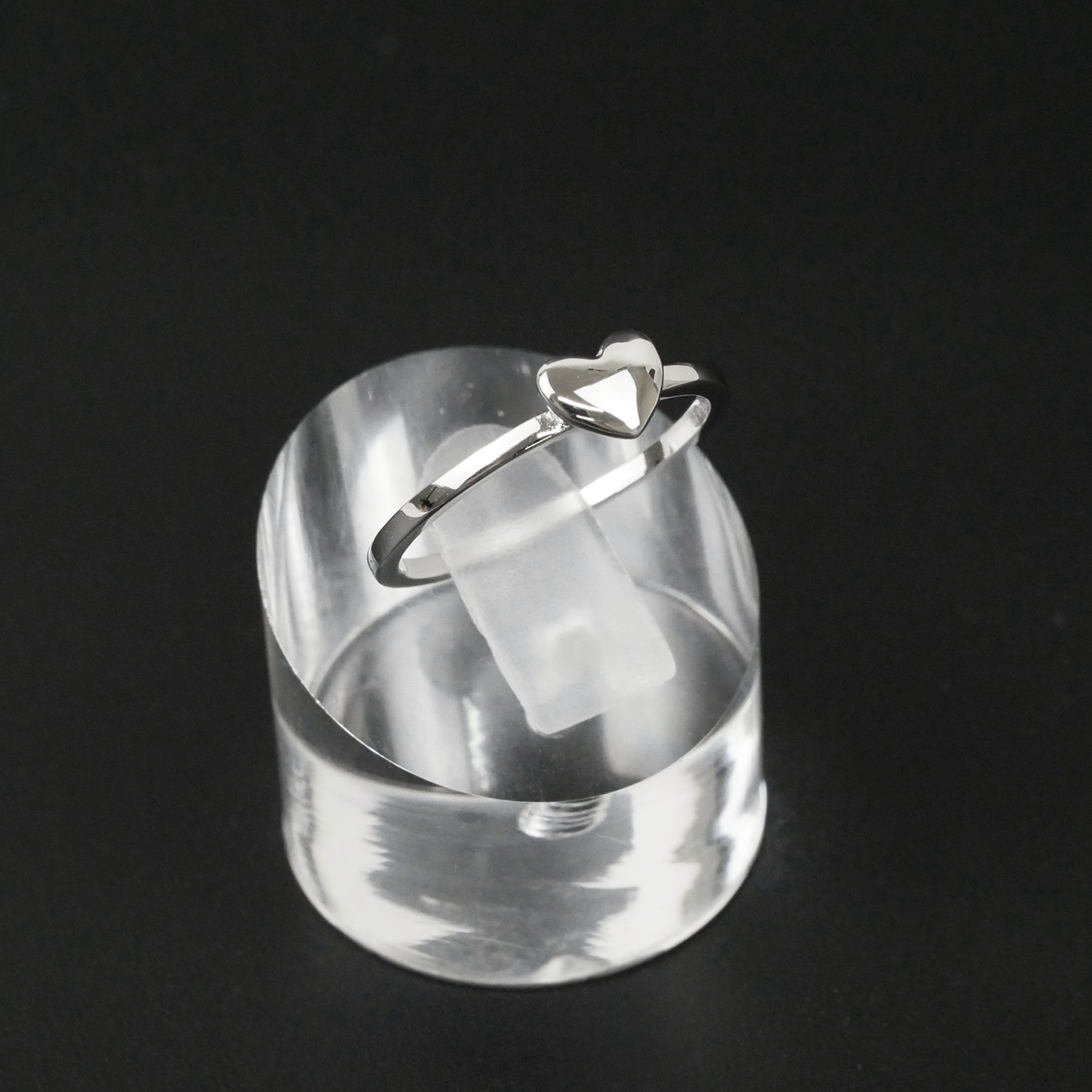 Silver ring with a heart design on a clear stand against a black background
