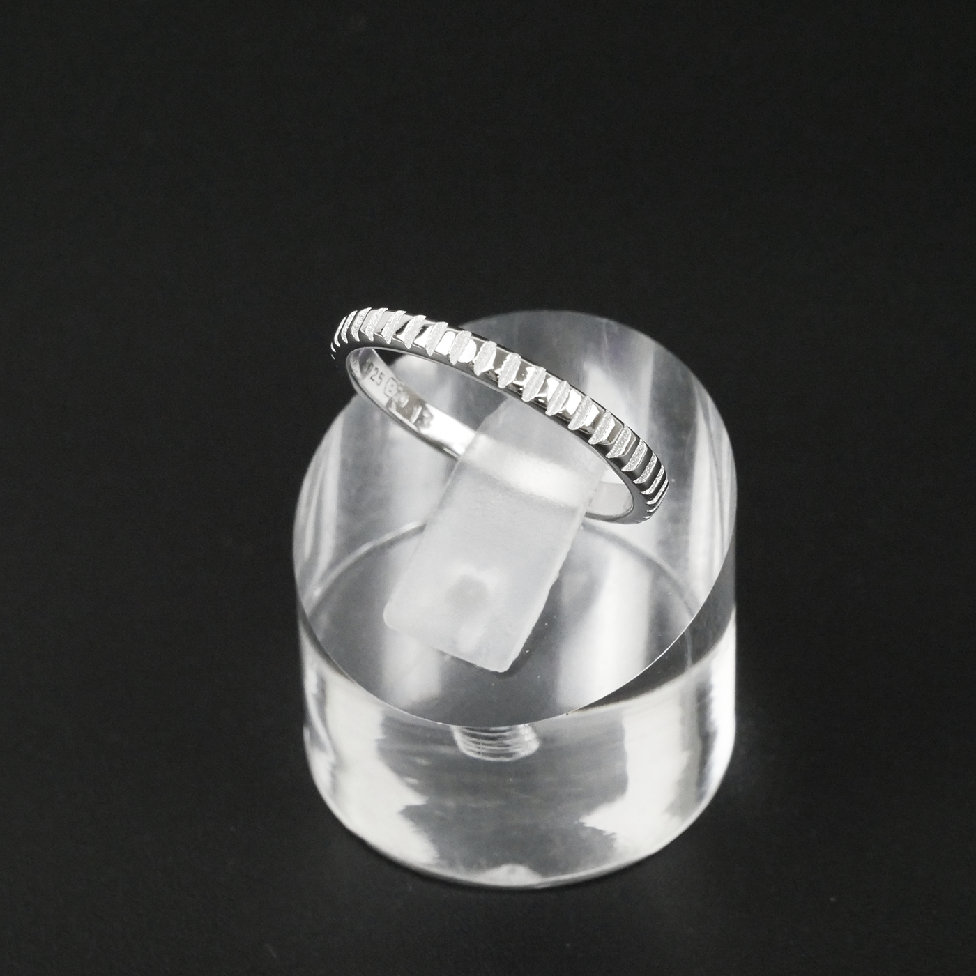 Silver ring on a clear stand against a black background