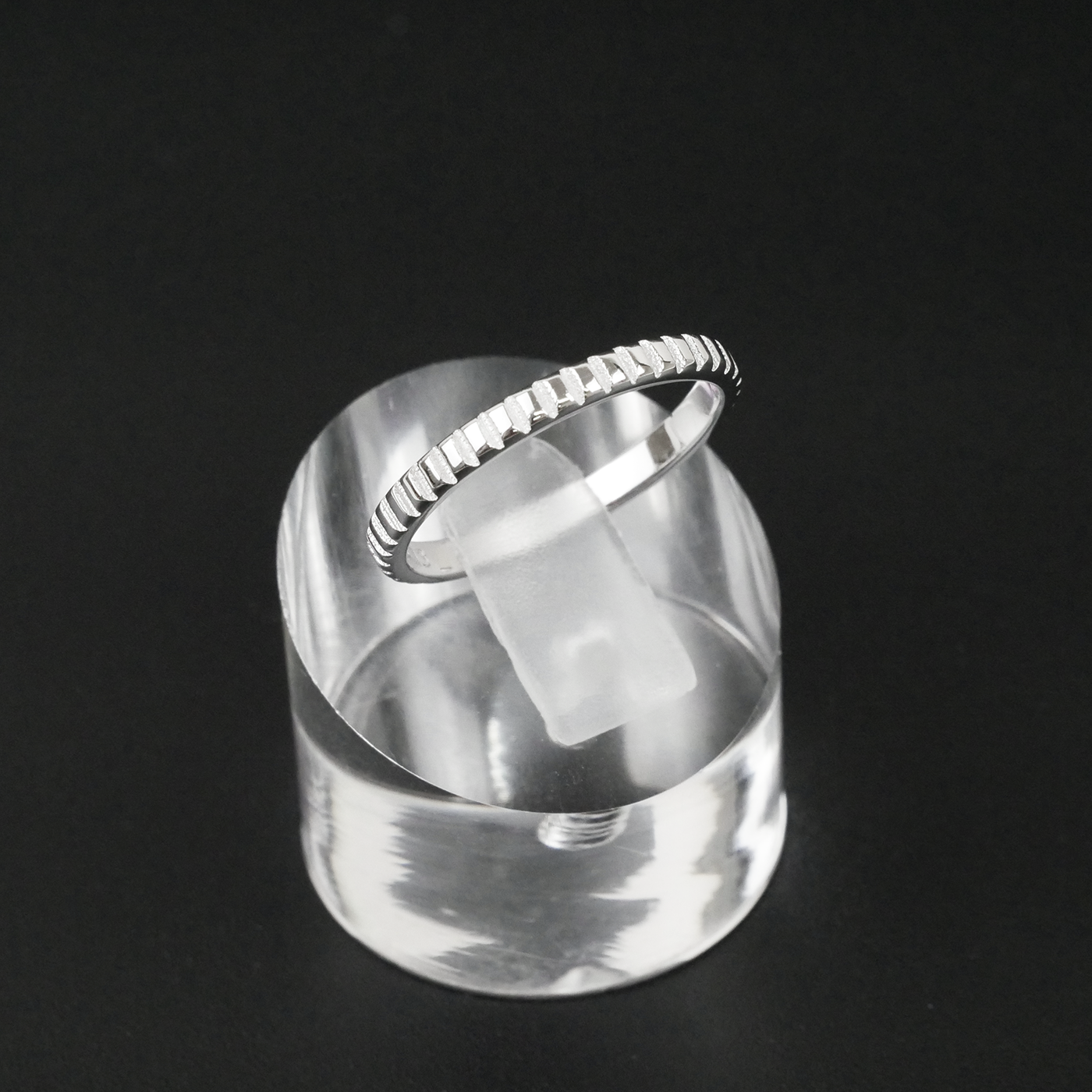 Silver ring on a clear stand against a black background