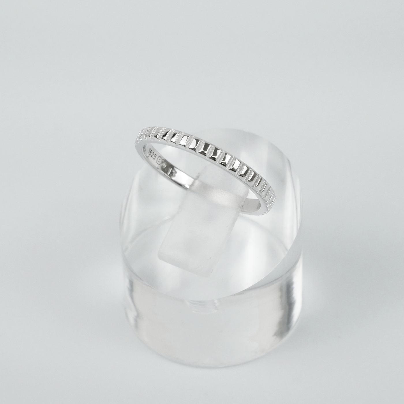Silver ring on a clear stand against a light gray background