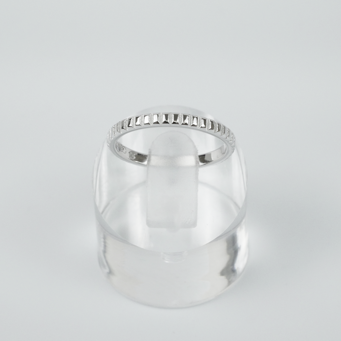 Silver ring on a clear stand against a light gray background