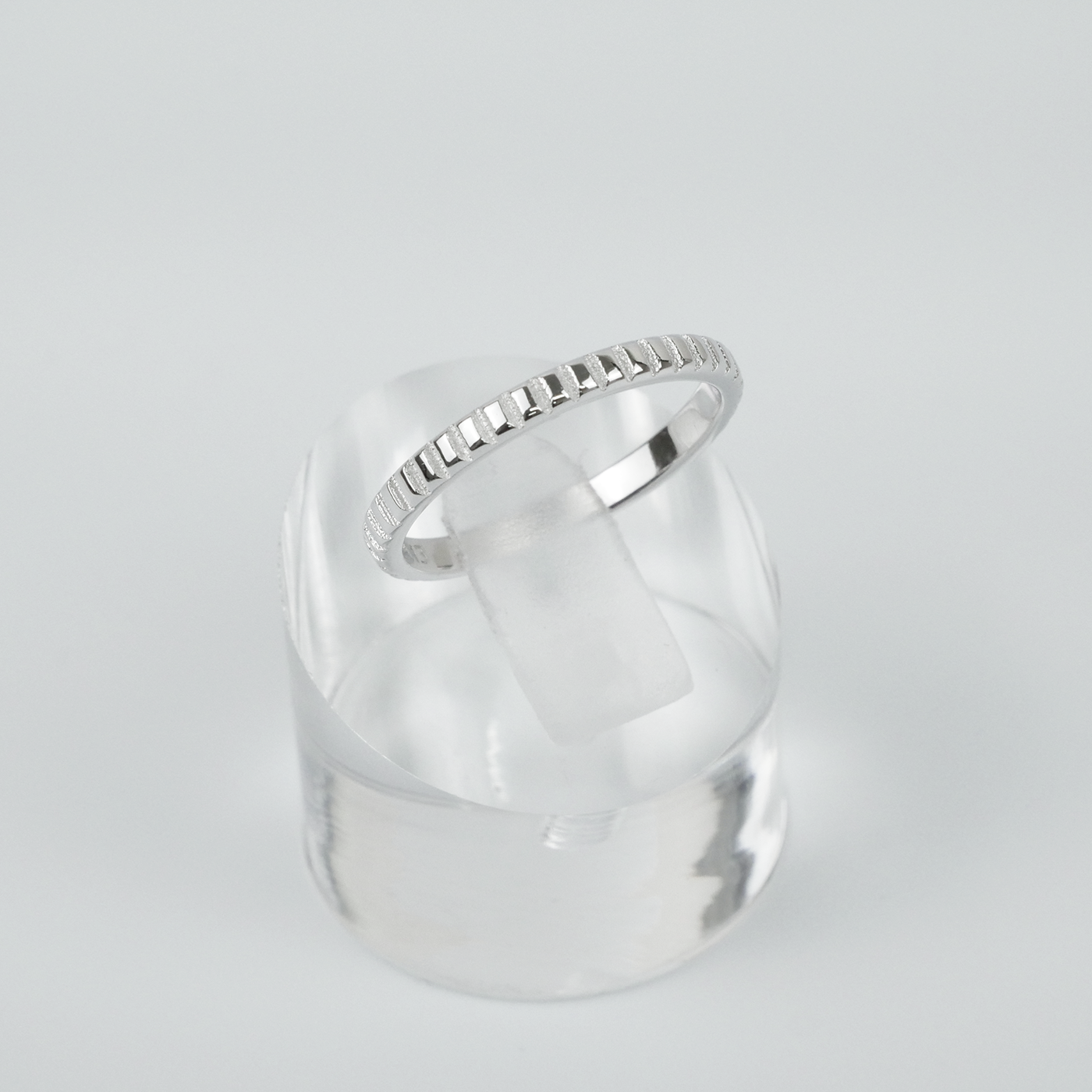 Silver ring on a clear stand against a light gray background