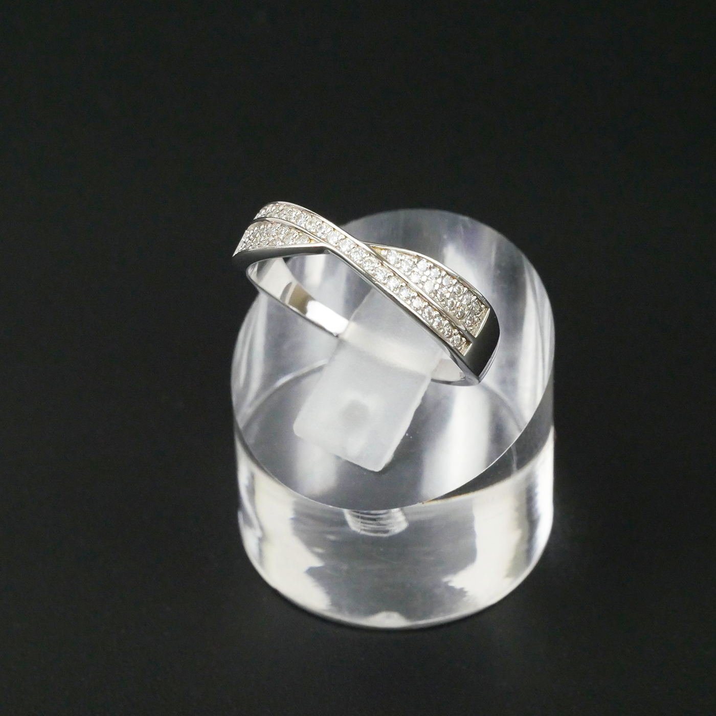 Silver ring with gemstone accents on a clear stand against a black background