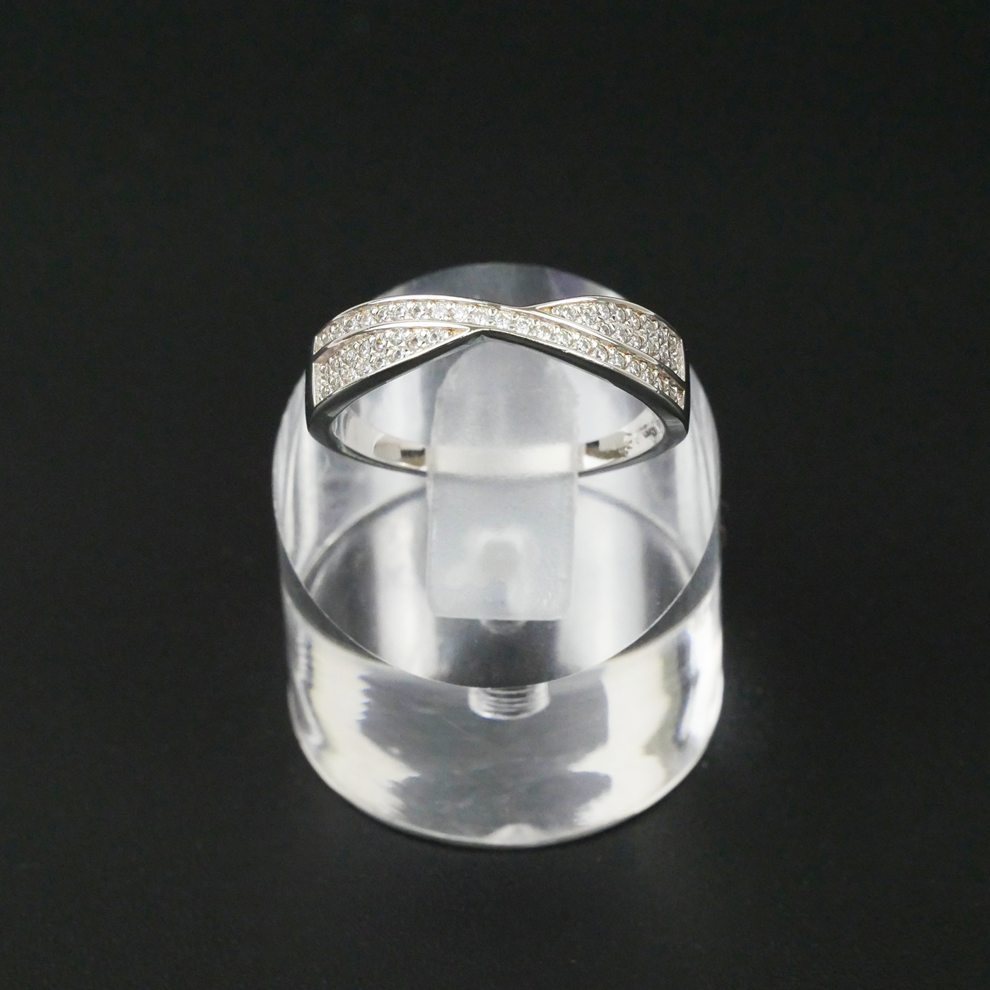 Silver ring with gemstone accents on a clear stand against a black background