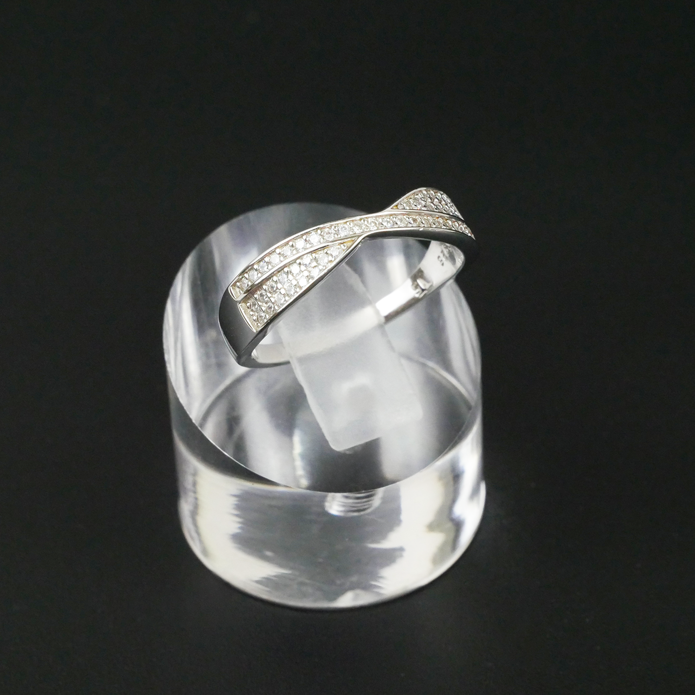 Silver ring with gemstone accents on a clear stand against a black background