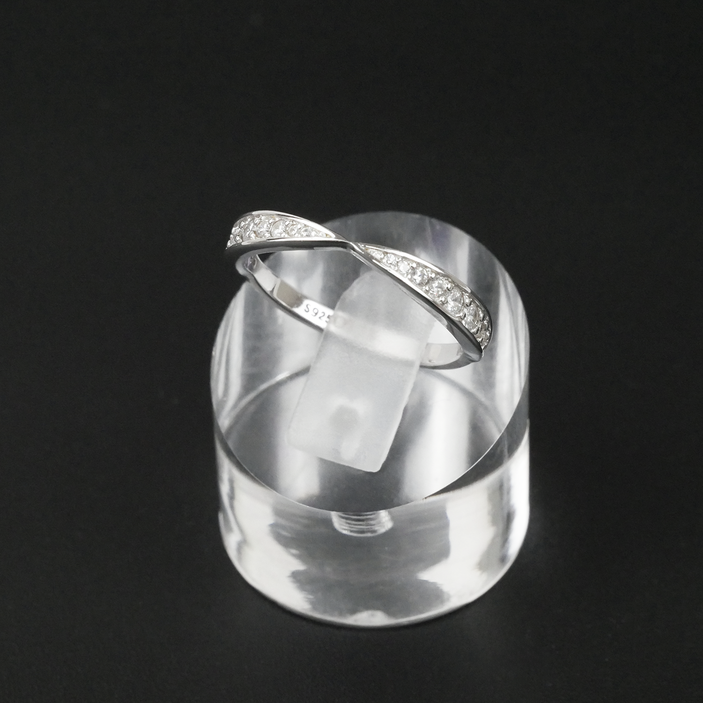 Silver ring with embedded gemstones on a clear stand against a black background