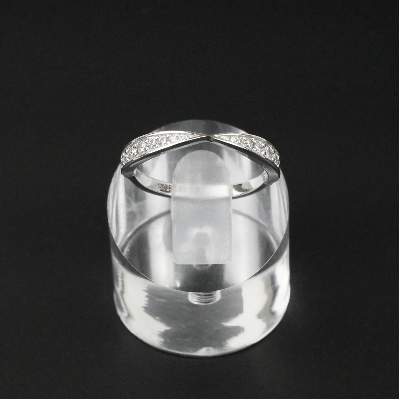 Silver ring with embedded gemstones on a clear stand against a black background