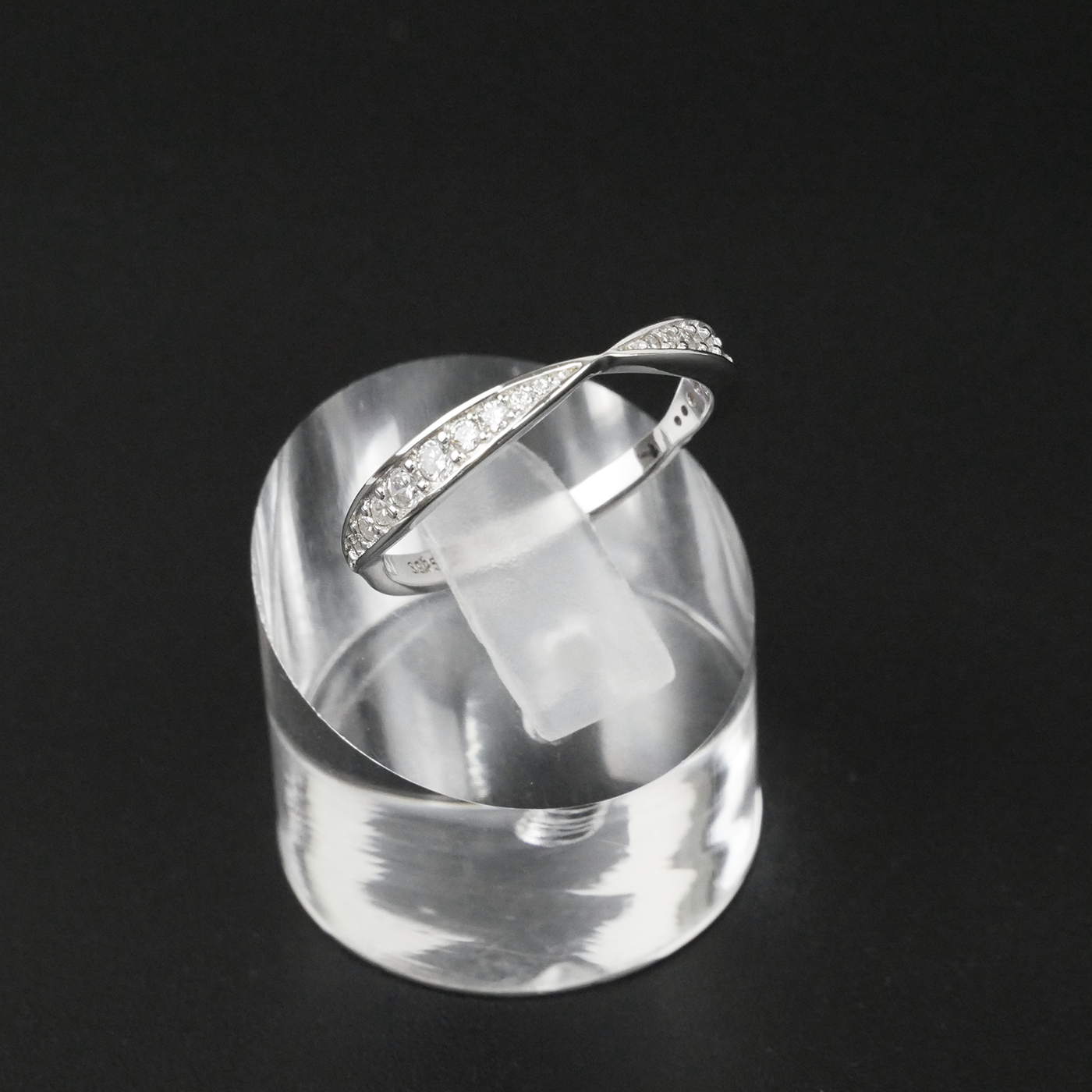Silver ring with embedded gemstones on a clear stand against a black background