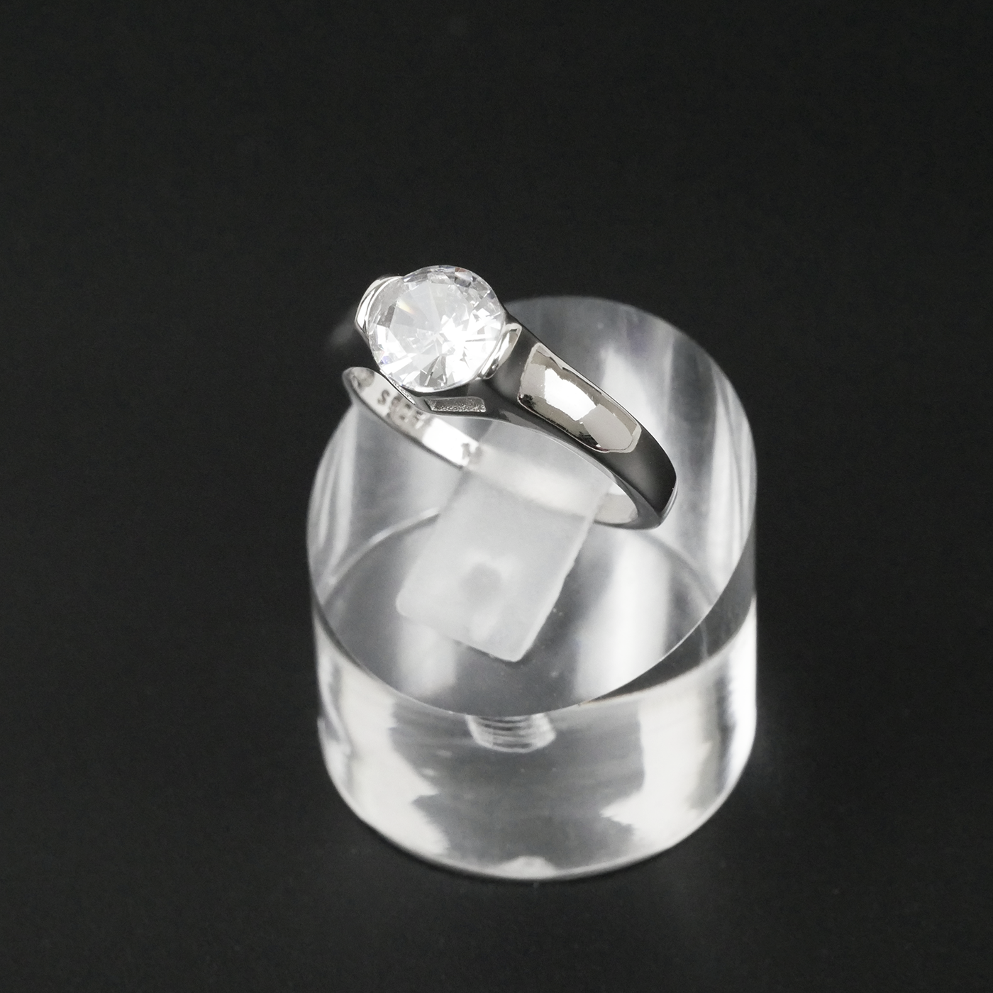 Silver ring with a gemstone on a clear stand against a black background