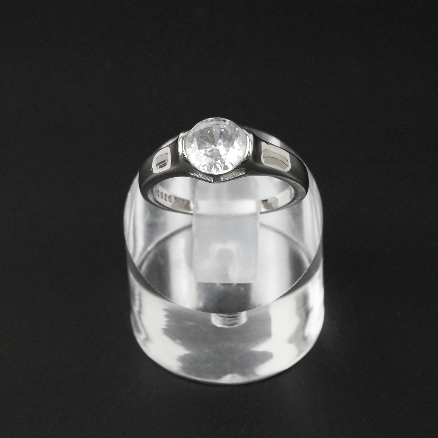 Silver ring with a gemstone on a clear stand against a black background
