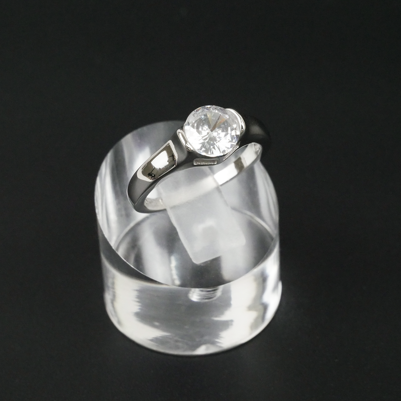 Silver ring with a gemstone on a clear stand against a black background