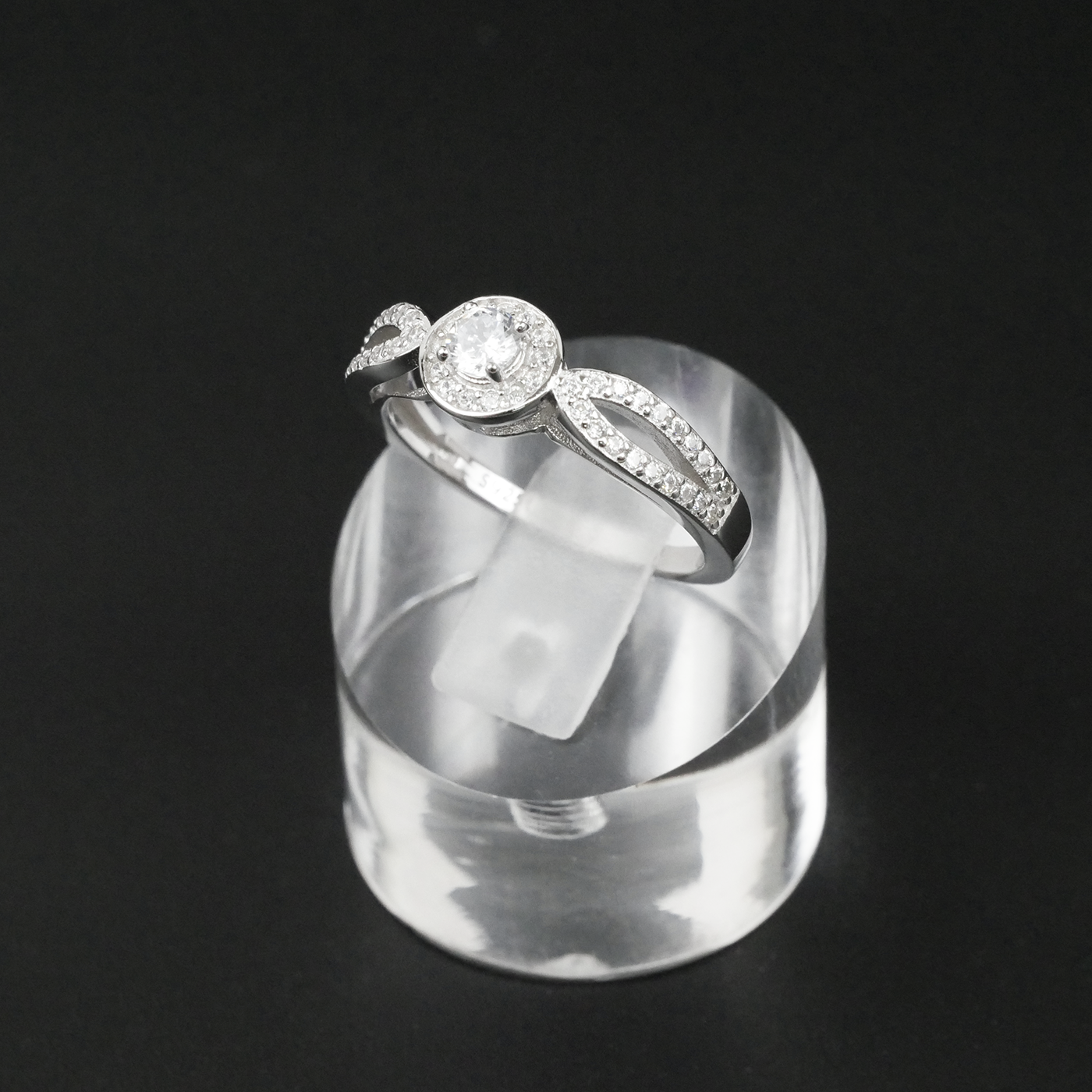 Silver ring with a clear gemstone on a clear stand against a black background