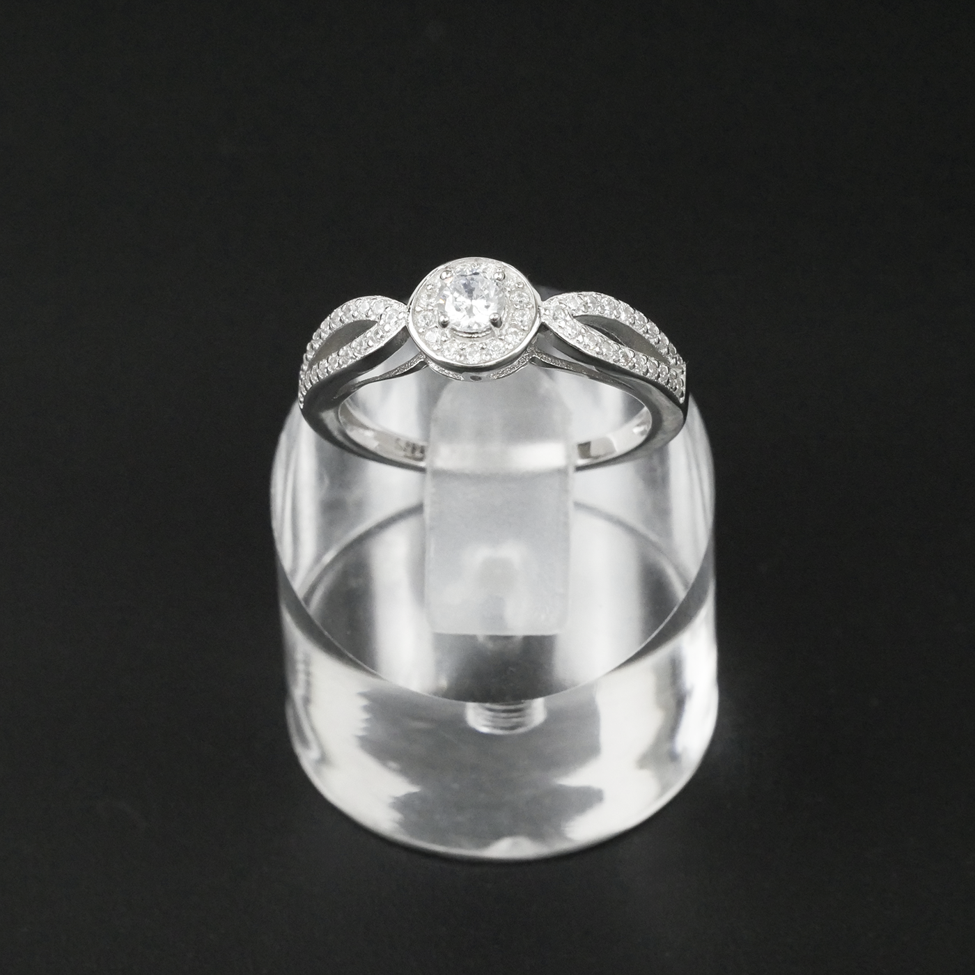 Silver ring with a clear gemstone on a clear stand against a black background