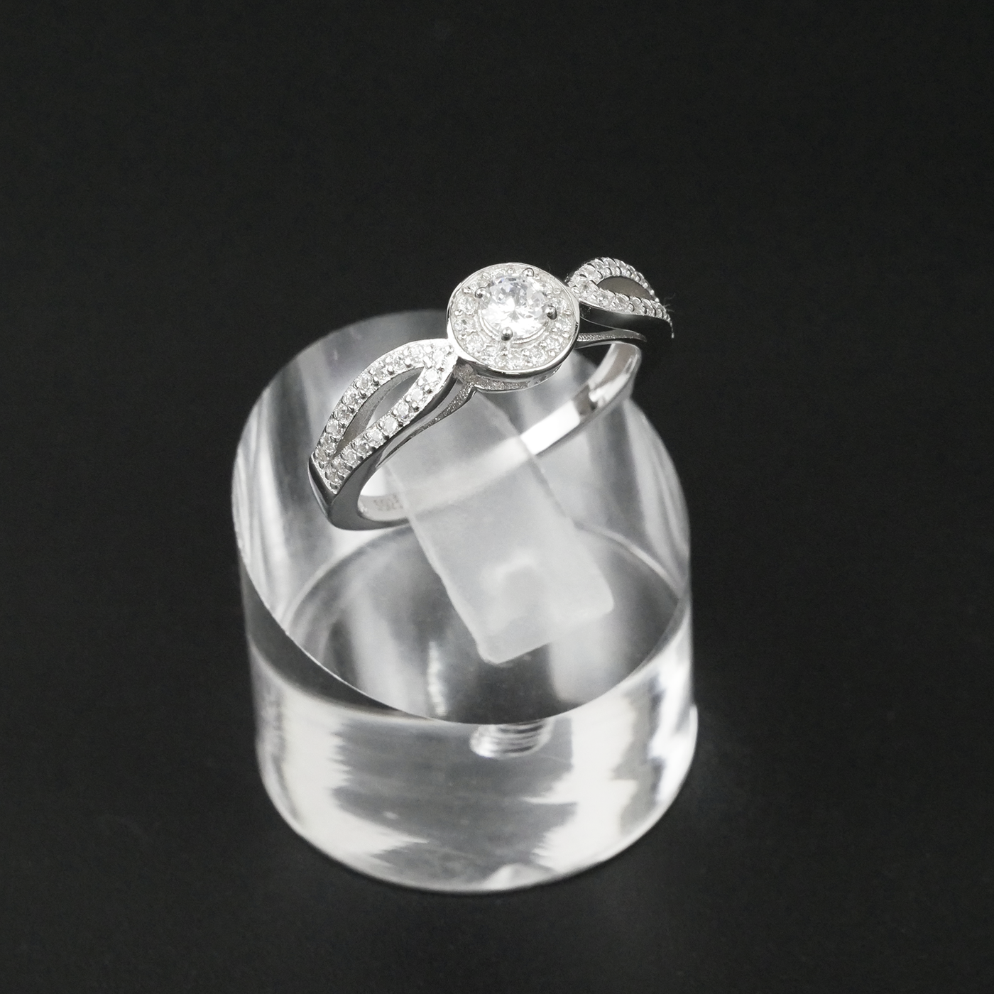 Silver ring with a clear gemstone on a clear stand against a black background