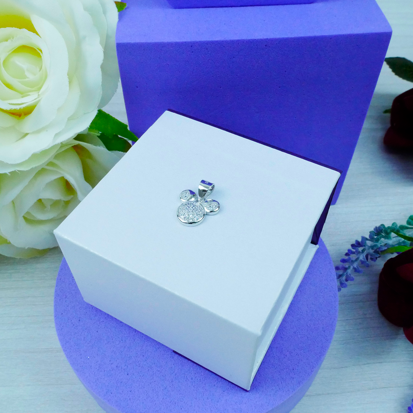 Silver turtle pendant in a white box on a purple stand with flowers in the background